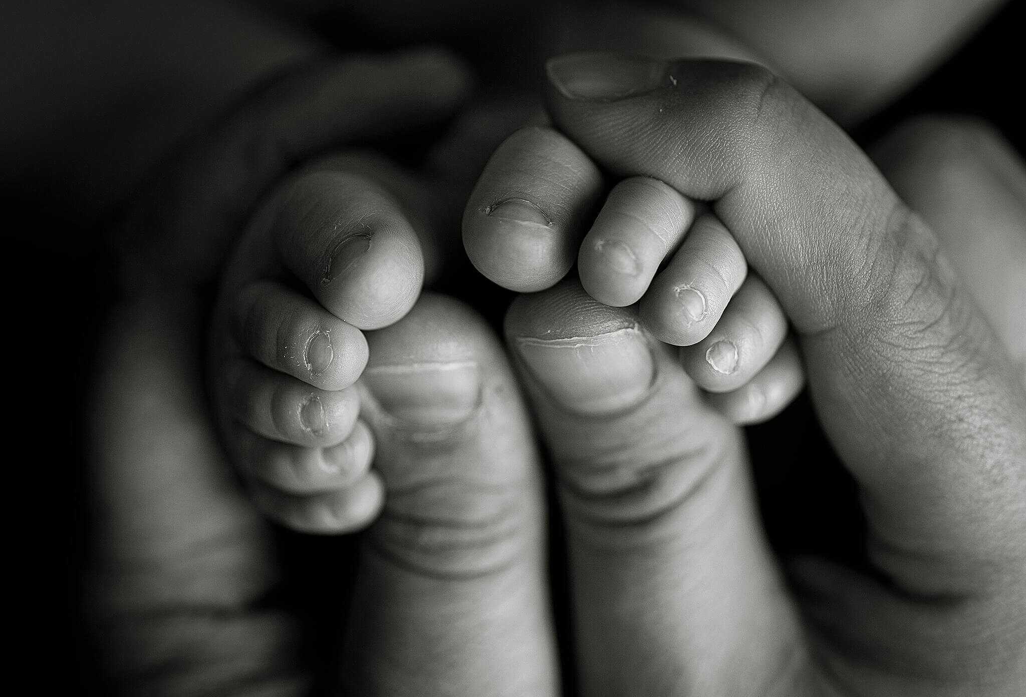 Black and white image of father holding newborn babies feet in his hands.