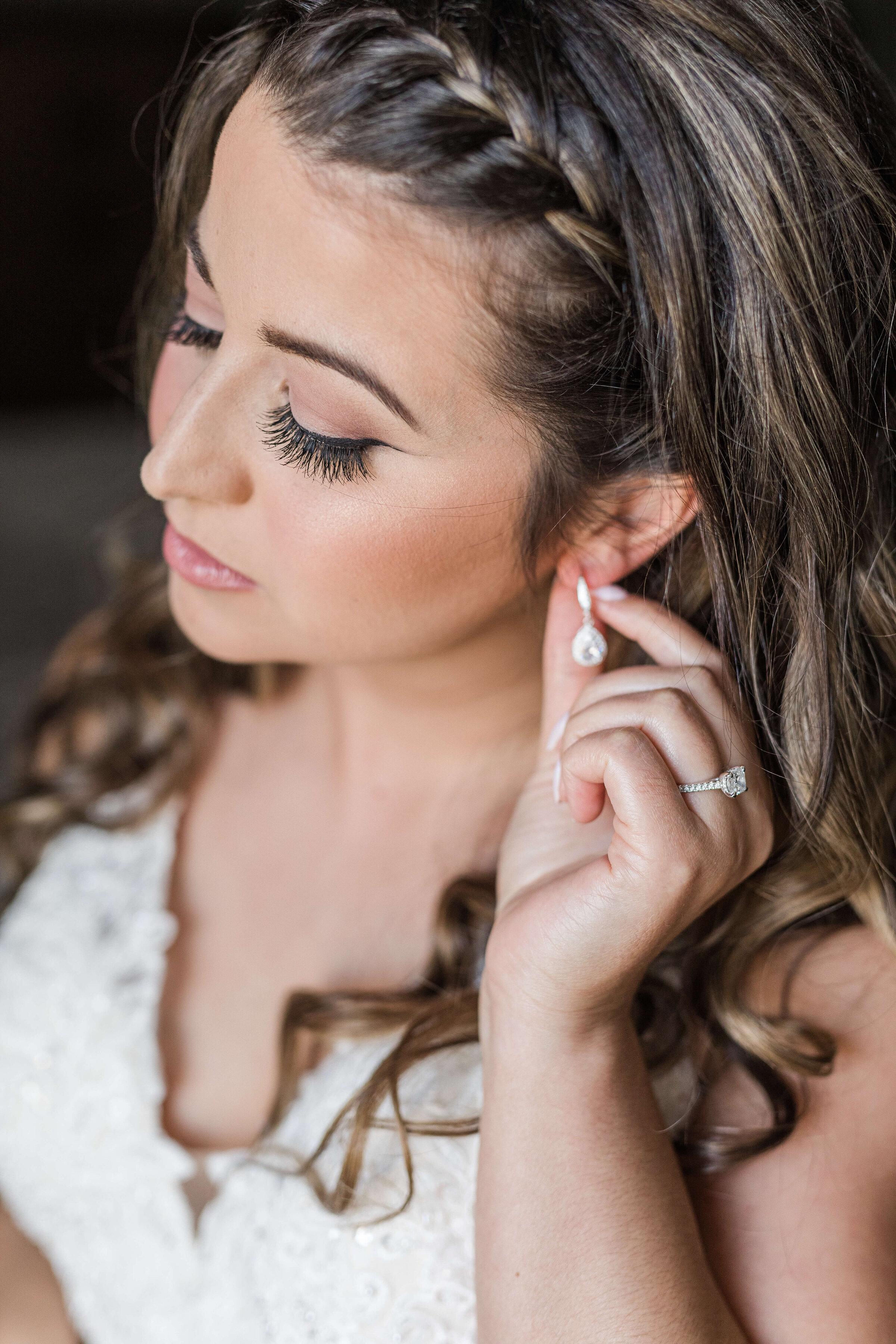 An up close photo of a bride putting on her earrings. Her makeup is done and she is looking toward the ground gracefully