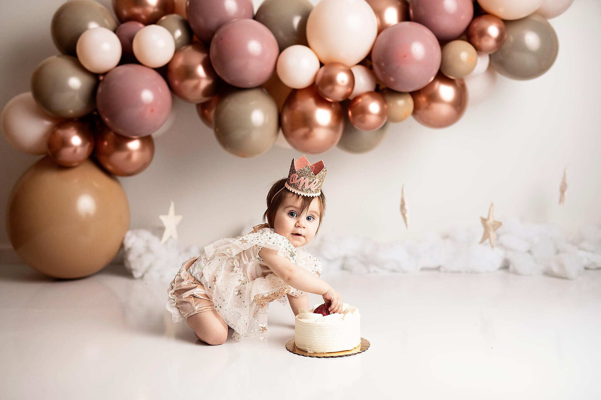 One year old in star outfit with cake and pink, brown and mauve ballon arches and stars in bucyrus ohio photography studio