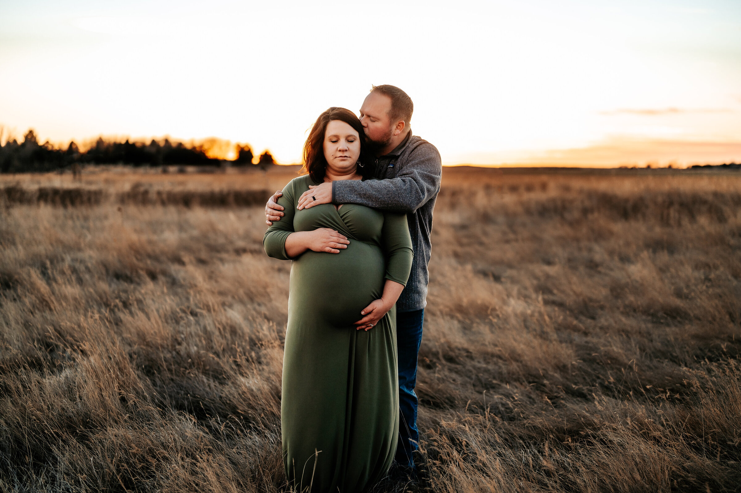 man hugs woman and kisses her forehead in maternity photos