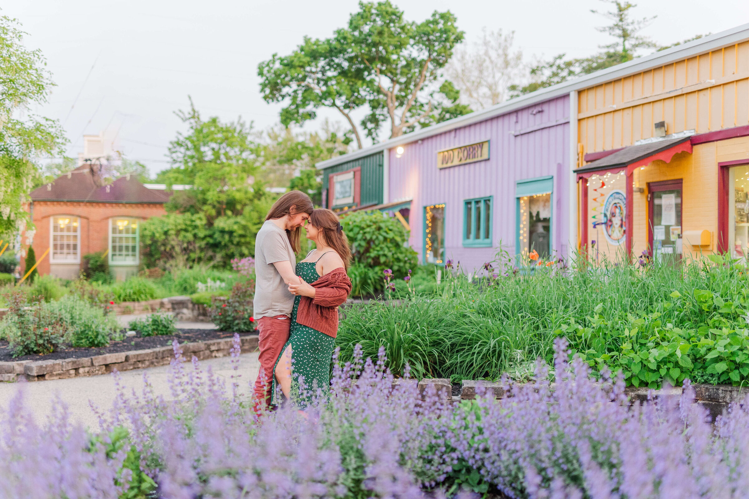 A man and woman hold each other in a garden of purple flowers. There is also a purple building in back of them. They are down in yellow springs ohio