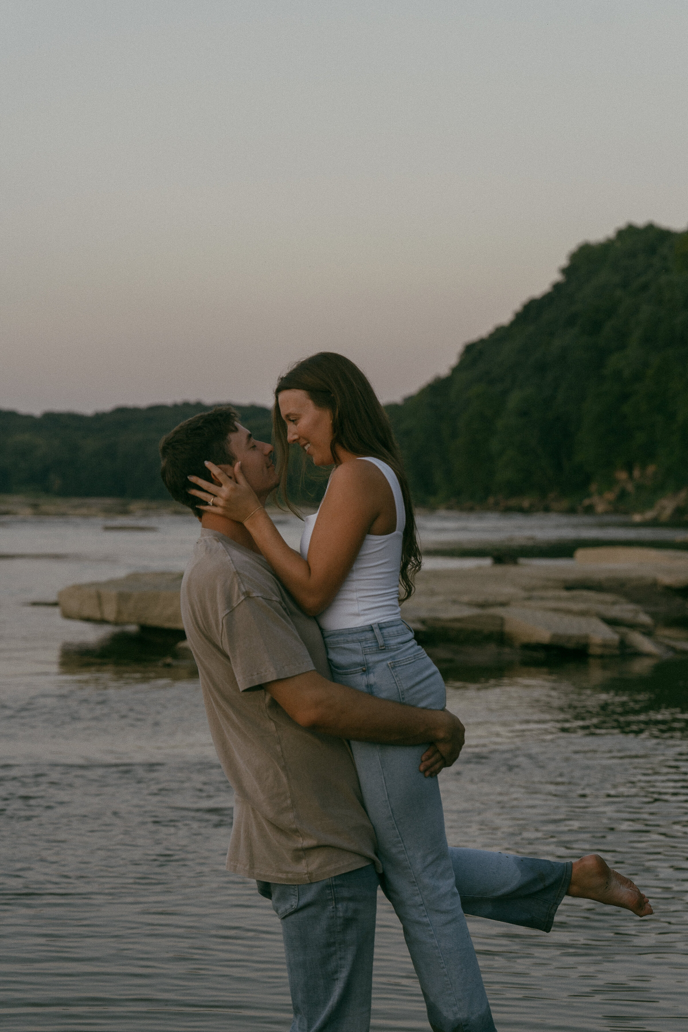 Couple embracing on a rocky riverbank at dusk.