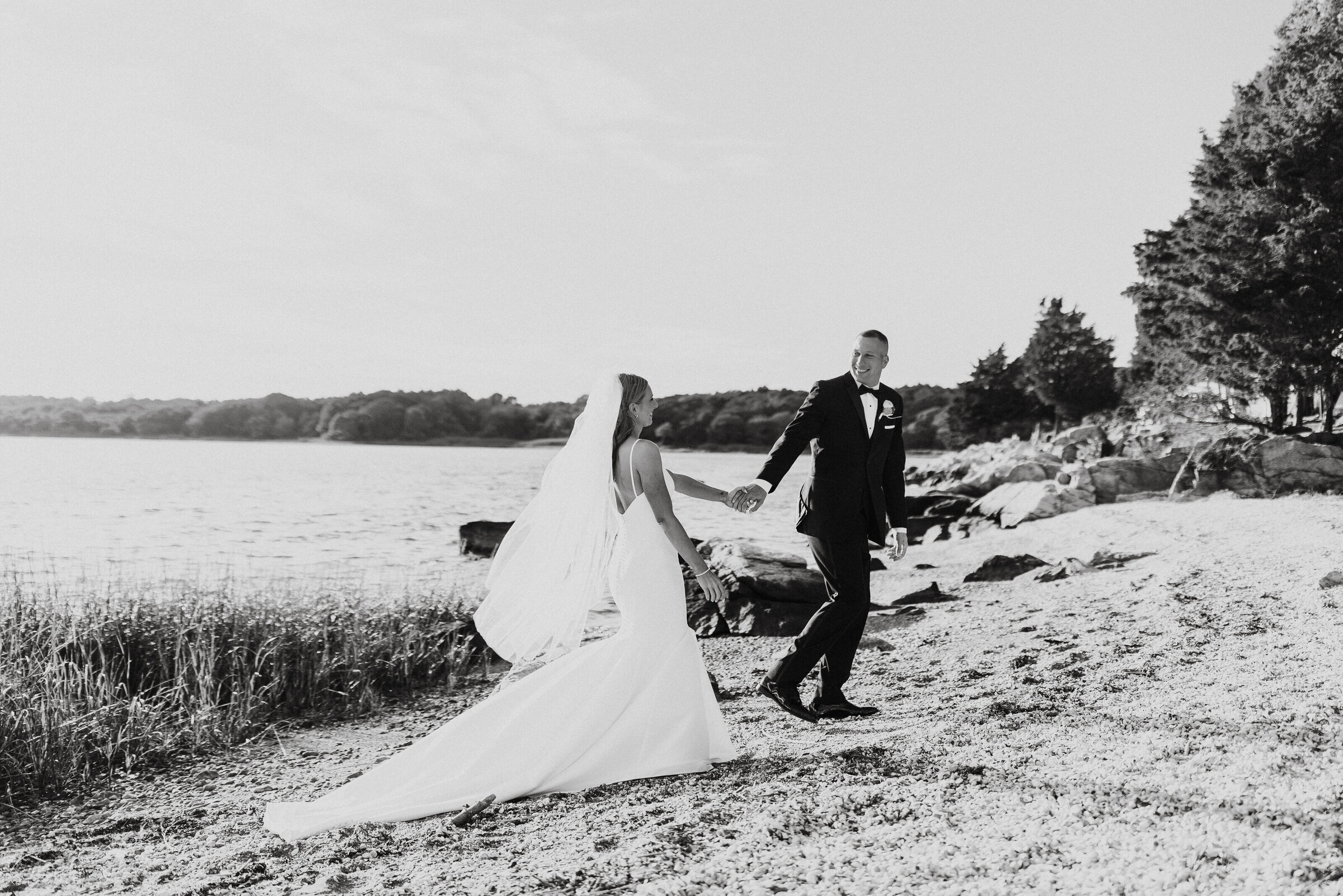 Bride and groom hold hands and walk along beach after wedding ceremony at Mount Hope Farm in Bristol, RI