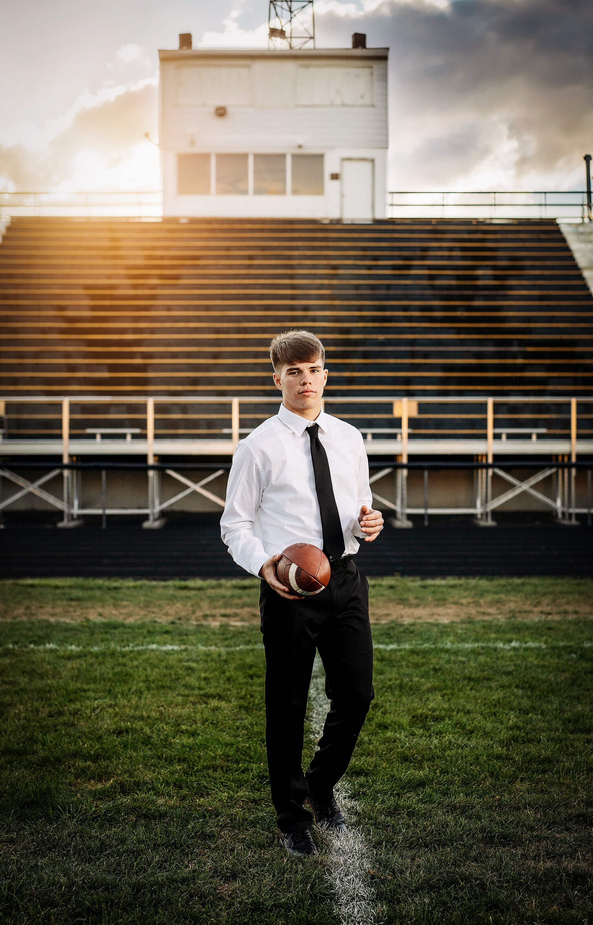 high school senior boy holding football while standing in front of football stands atColonel Crawford High school