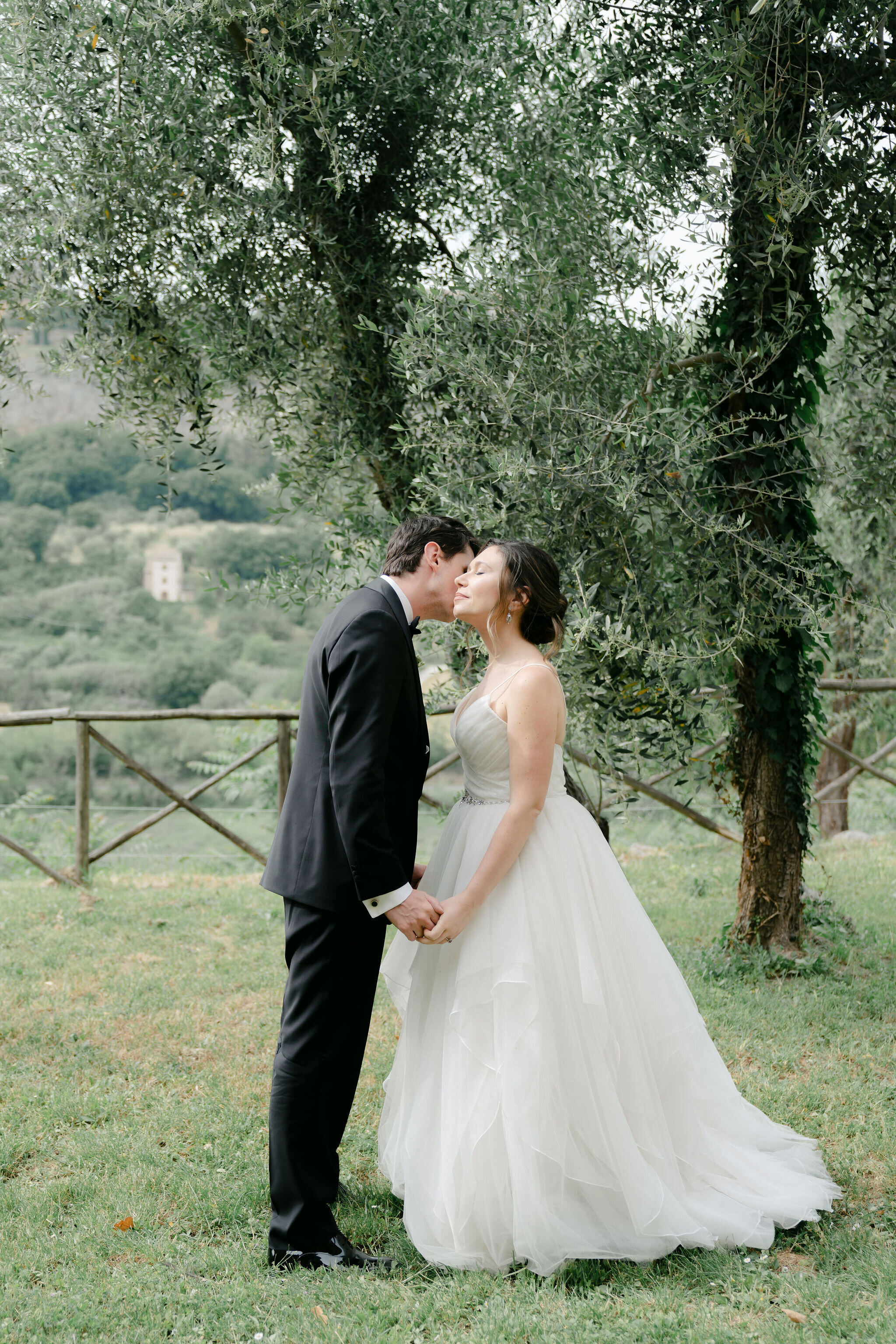 A bride and groom have a first look and kiss by the olive trees of La Badia di Orvieto