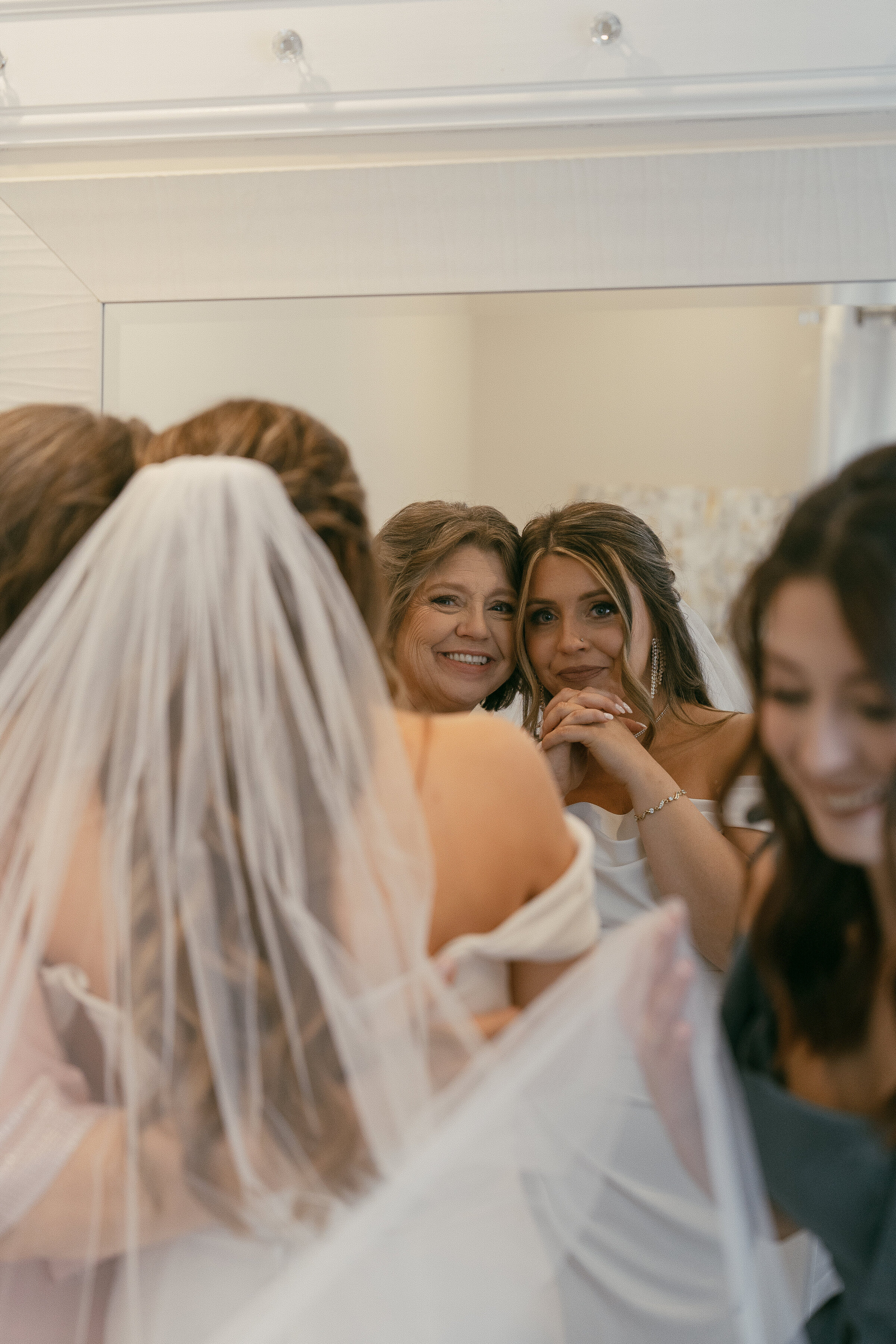 Mother and bride smiling in the mirror, a tender moment during wedding preparations.