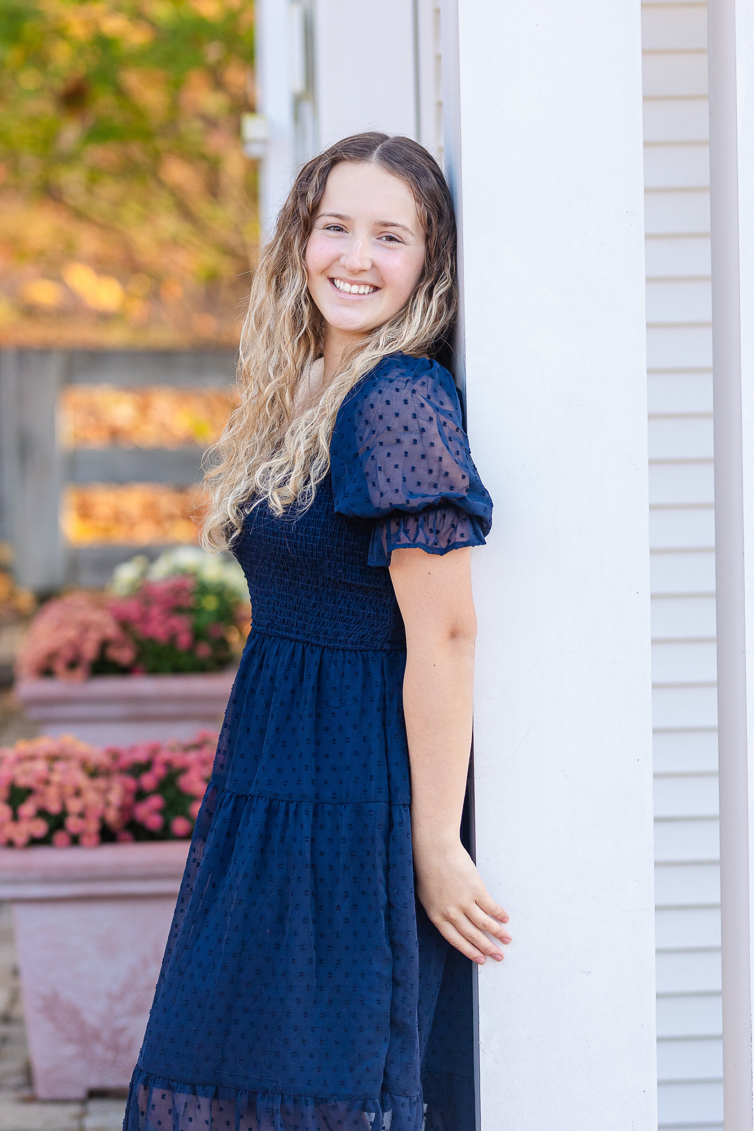senior girl wearing a long blue dress leaning against a post for her senior photos