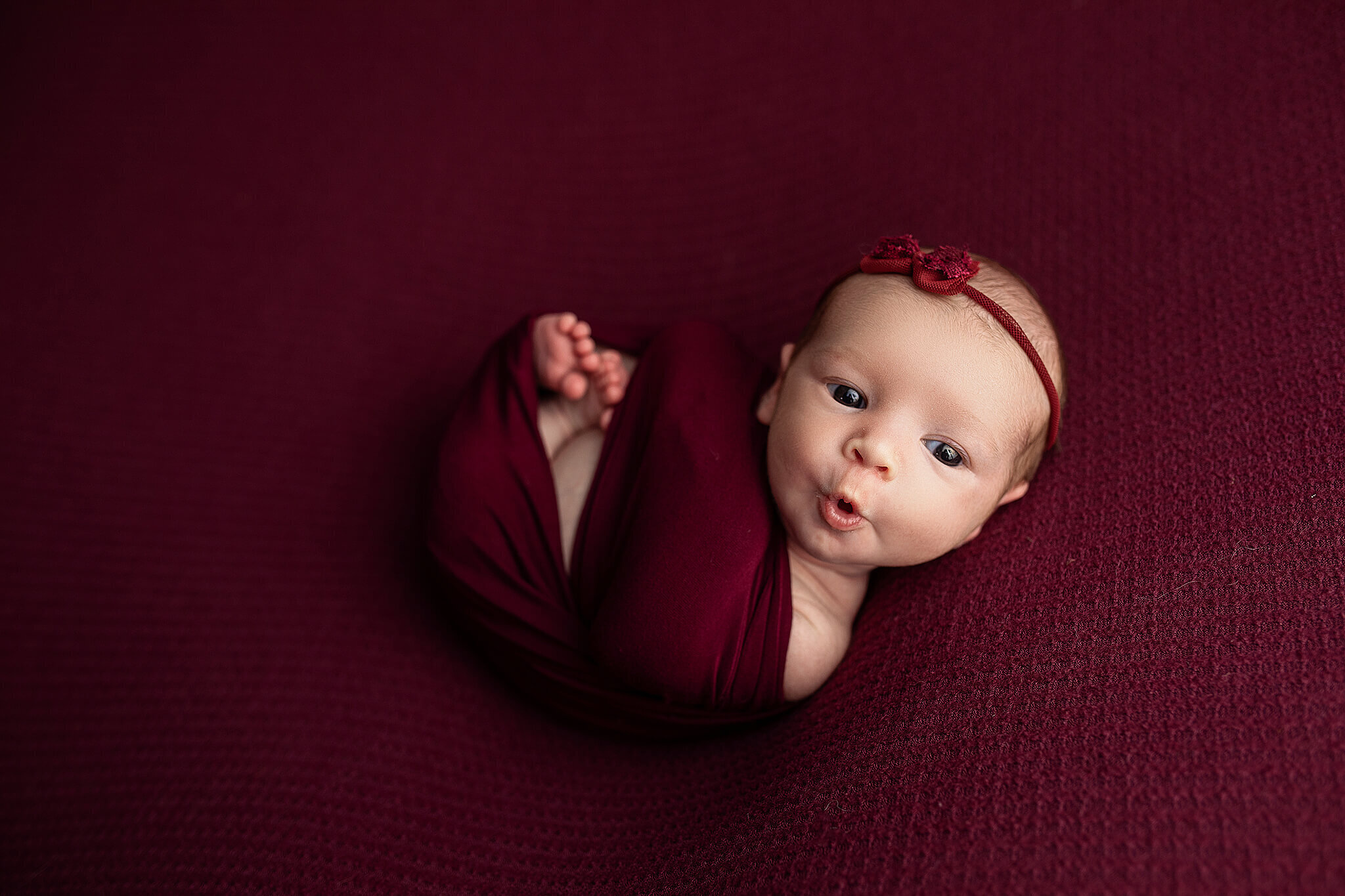 Newborn baby girl swaddled in scarlet wrap on a scarlet blanket