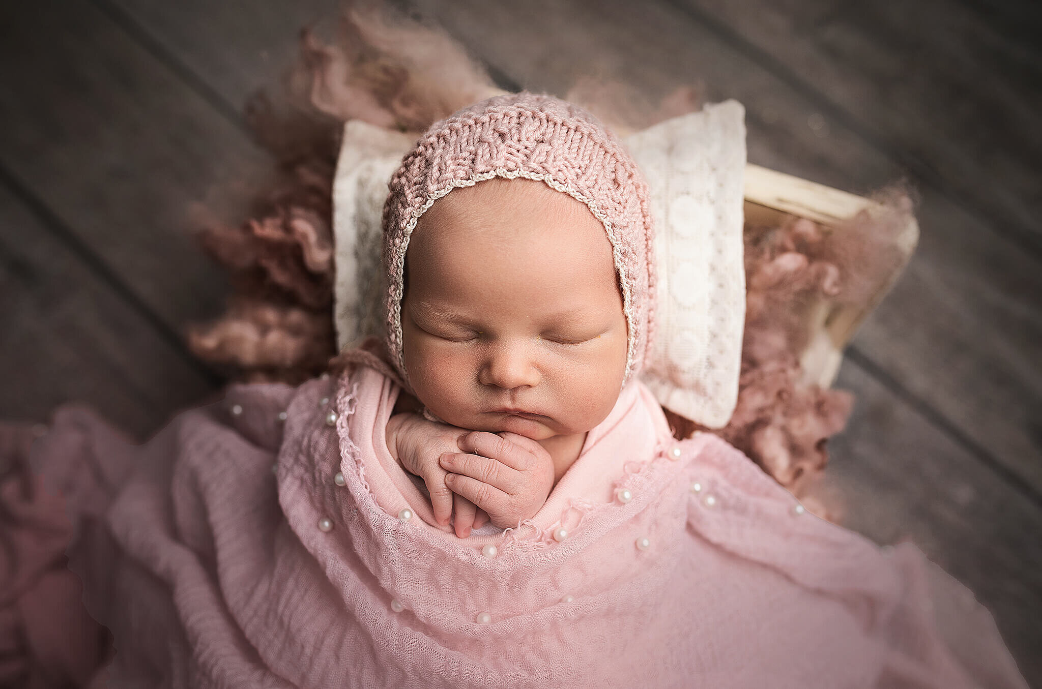 newborn girl in little white bed covered with cute pink blanket with pearls and a little pink knit hat