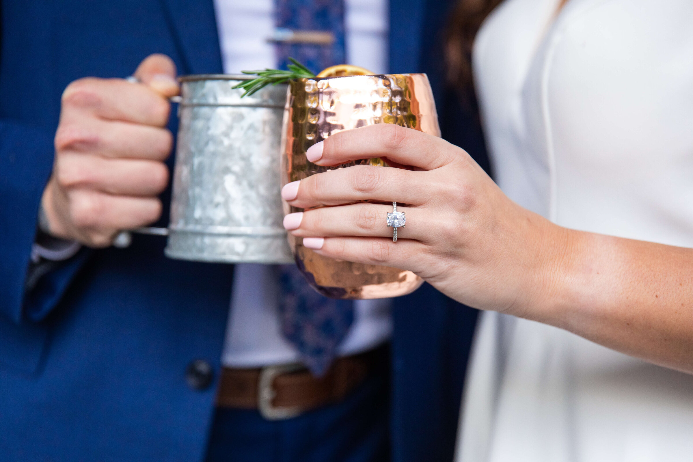 A bride and groom holding moscow mule mugs and the photo is up close of their hands showing the bride's ring.