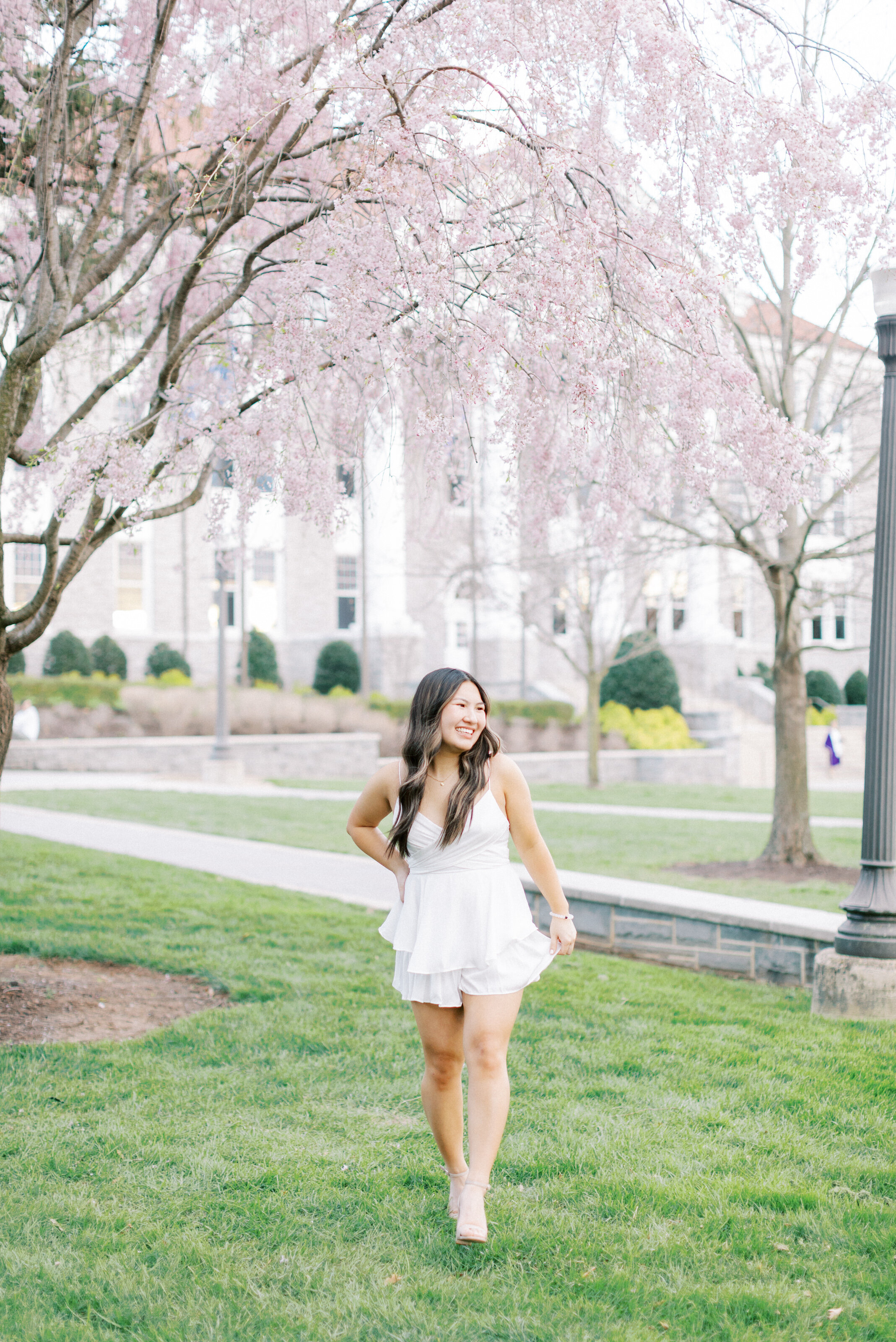 James Madison University Senior in a white dress walking on the Quad in Harrisonburg, VA.