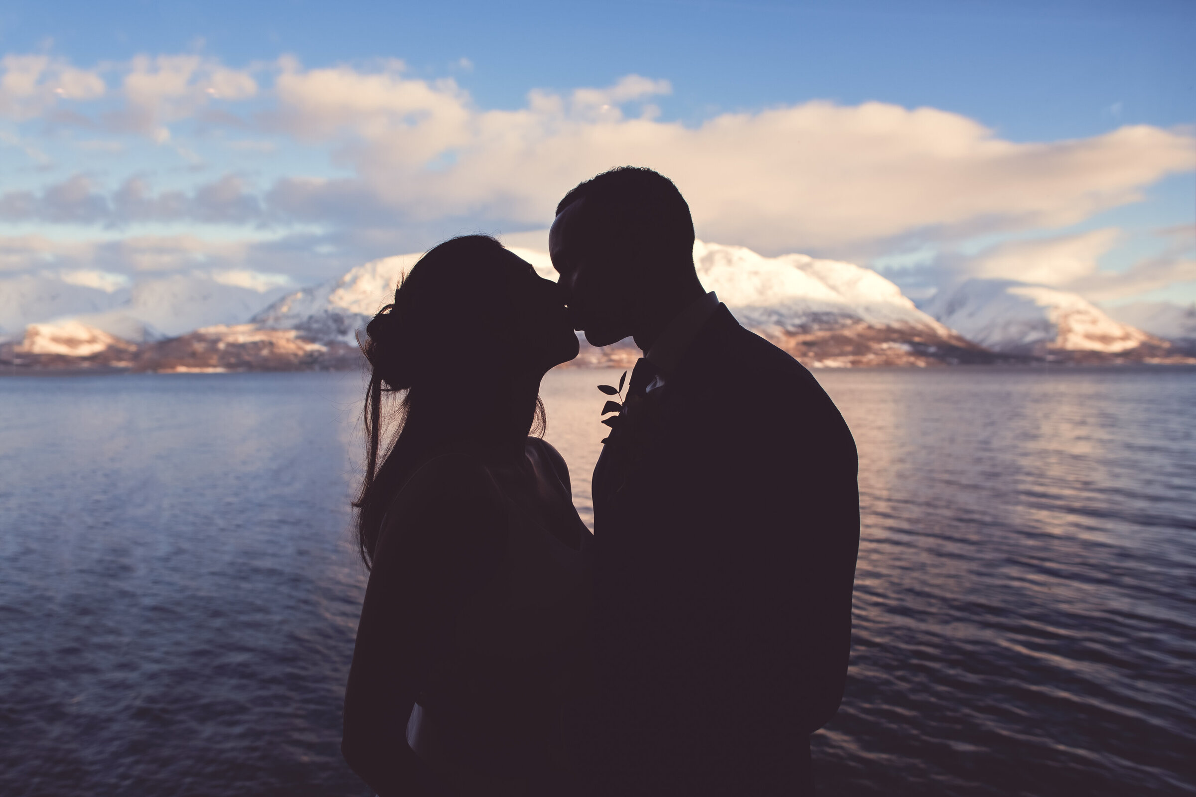 A couple silhouetted against a sunset in Tromsø, Norway, sharing a kiss with mountains in the distance, a romantic elopement moment captured in time.