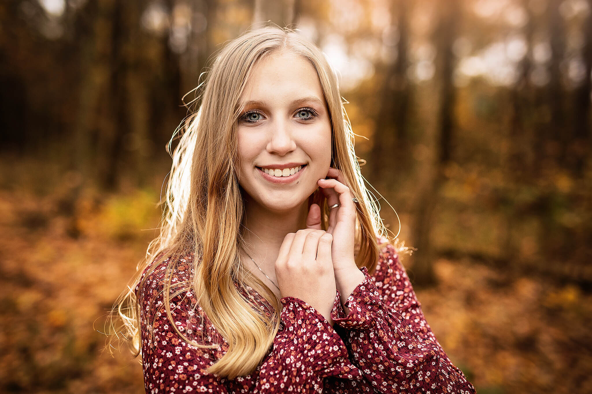 high school senior girl with blonde hair and red shirt with her hands posed up next to her face at lowe volk park