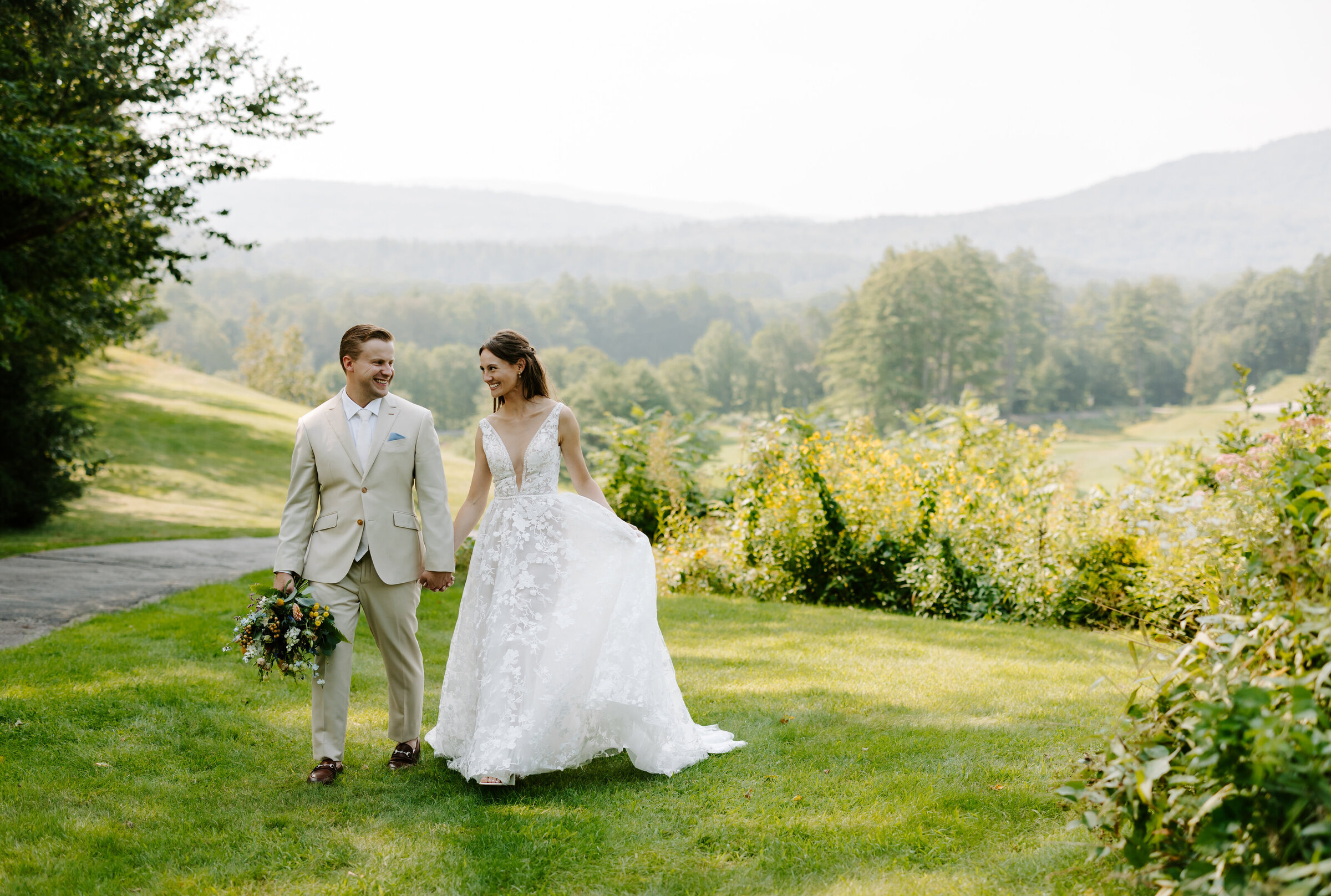Bride and groom hold hands and walk towards the camera on golf course after wedding ceremony at The Owl's Nest Resort in Thorton, NH