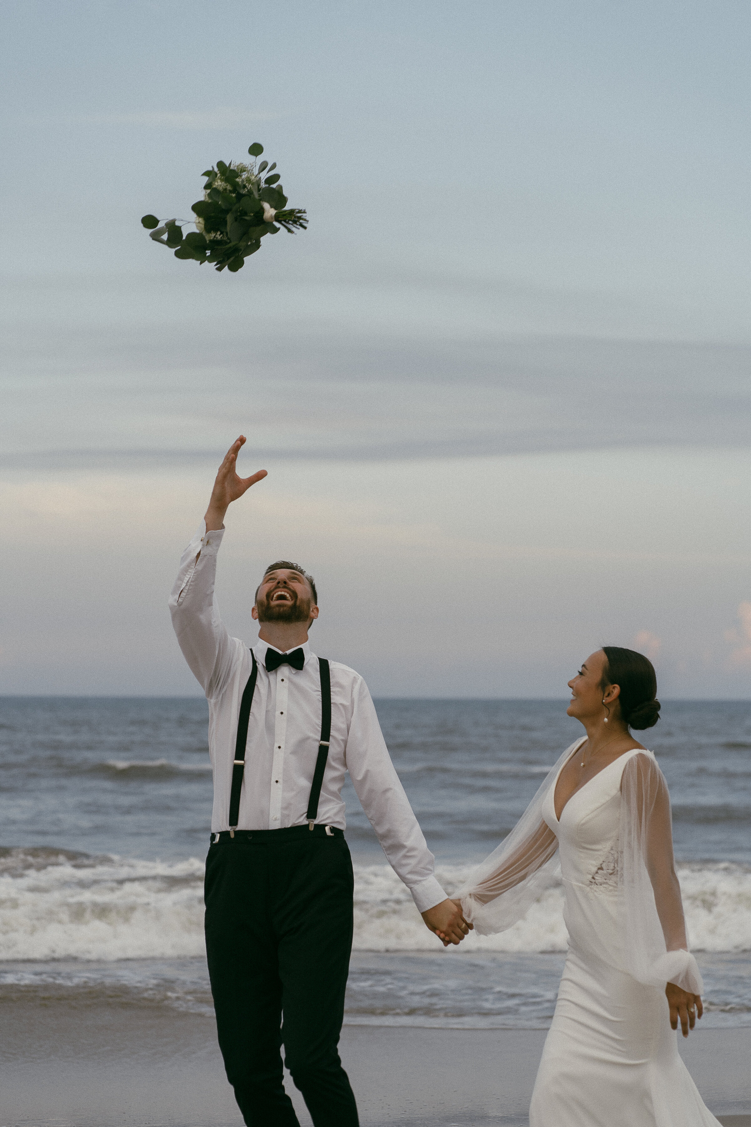 Bride and groom tossing a bouquet into the air on the beach.