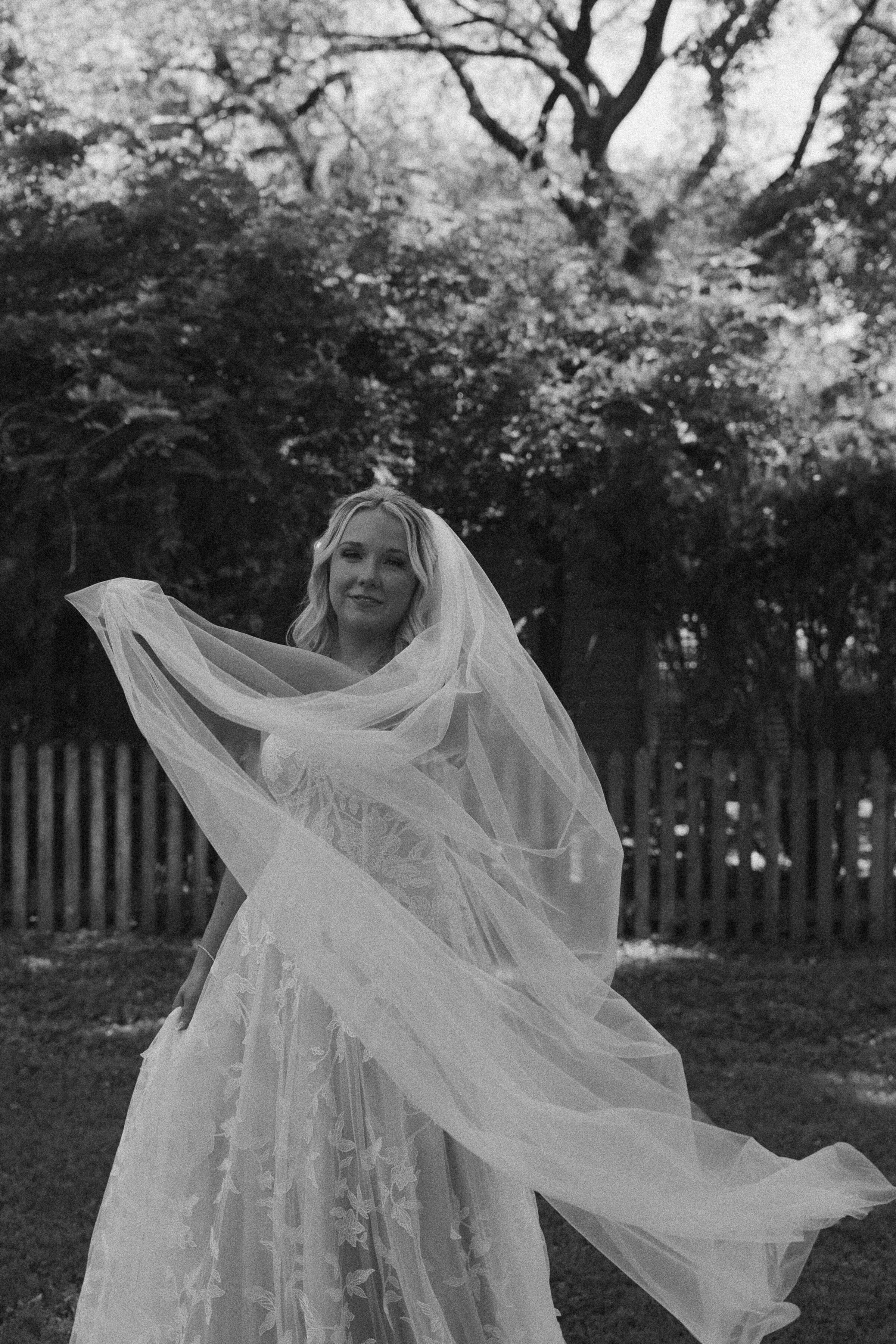 Black and white photo of a bride with veil in a garden.