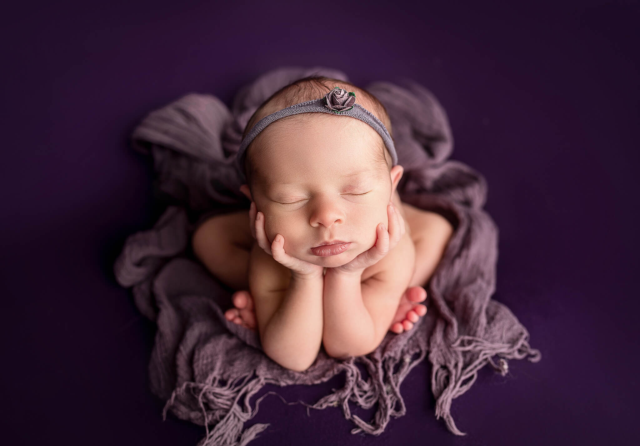 Newborn baby girl on purple blanket in froggy position
