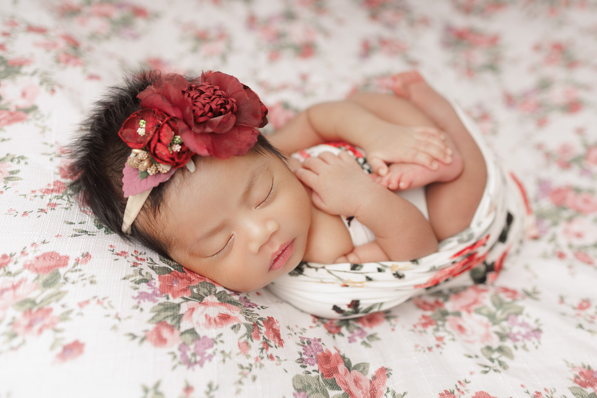 baby girl wrapped in floral blanket, wearing red floral headband