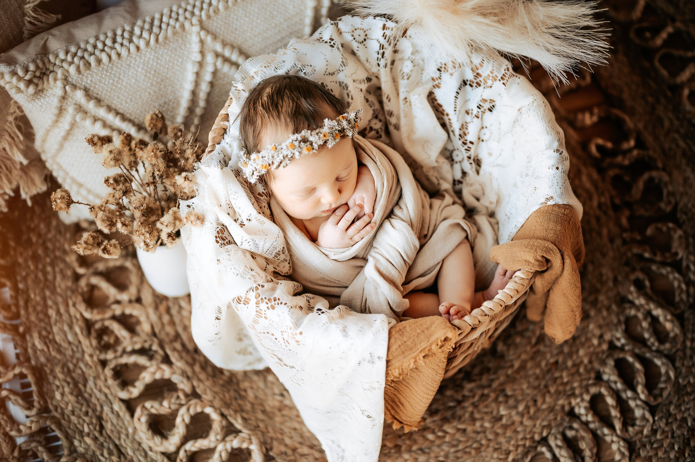 Newborn sits in basket in swaddle on rattan rug with boho props