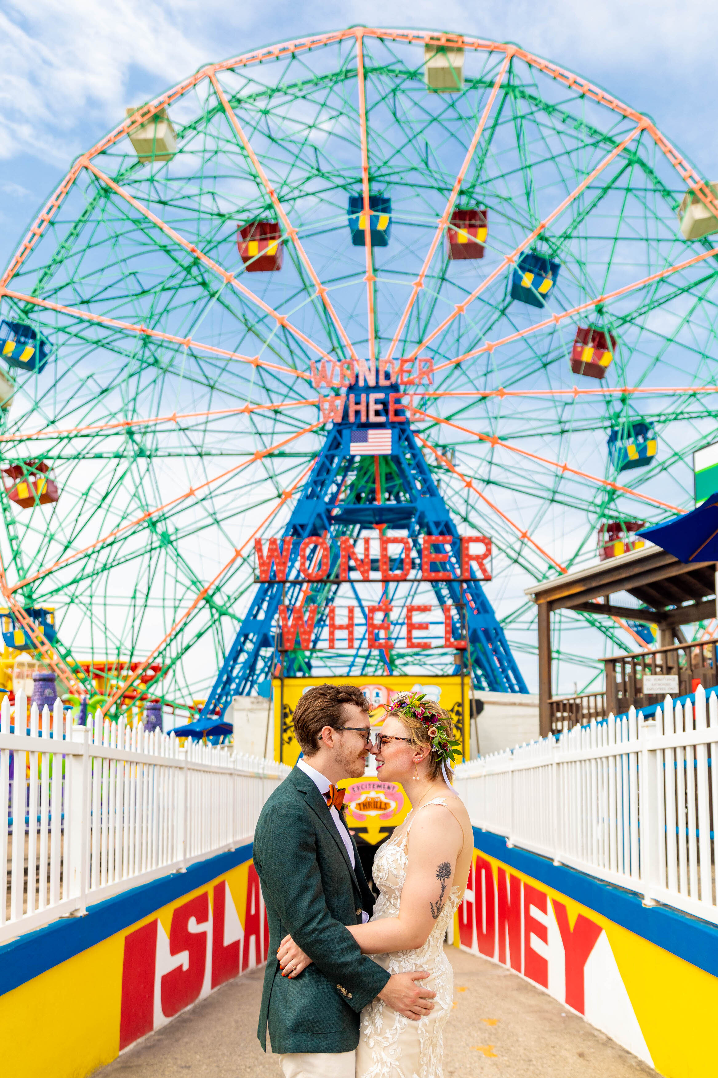 A couple with their arms around each other in front of a ferris wheel.