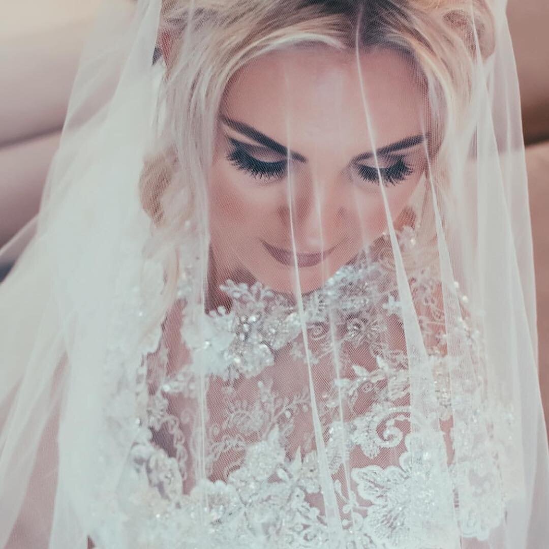 A woman  in her wedding  dress, looking down, with  her veil over her face.