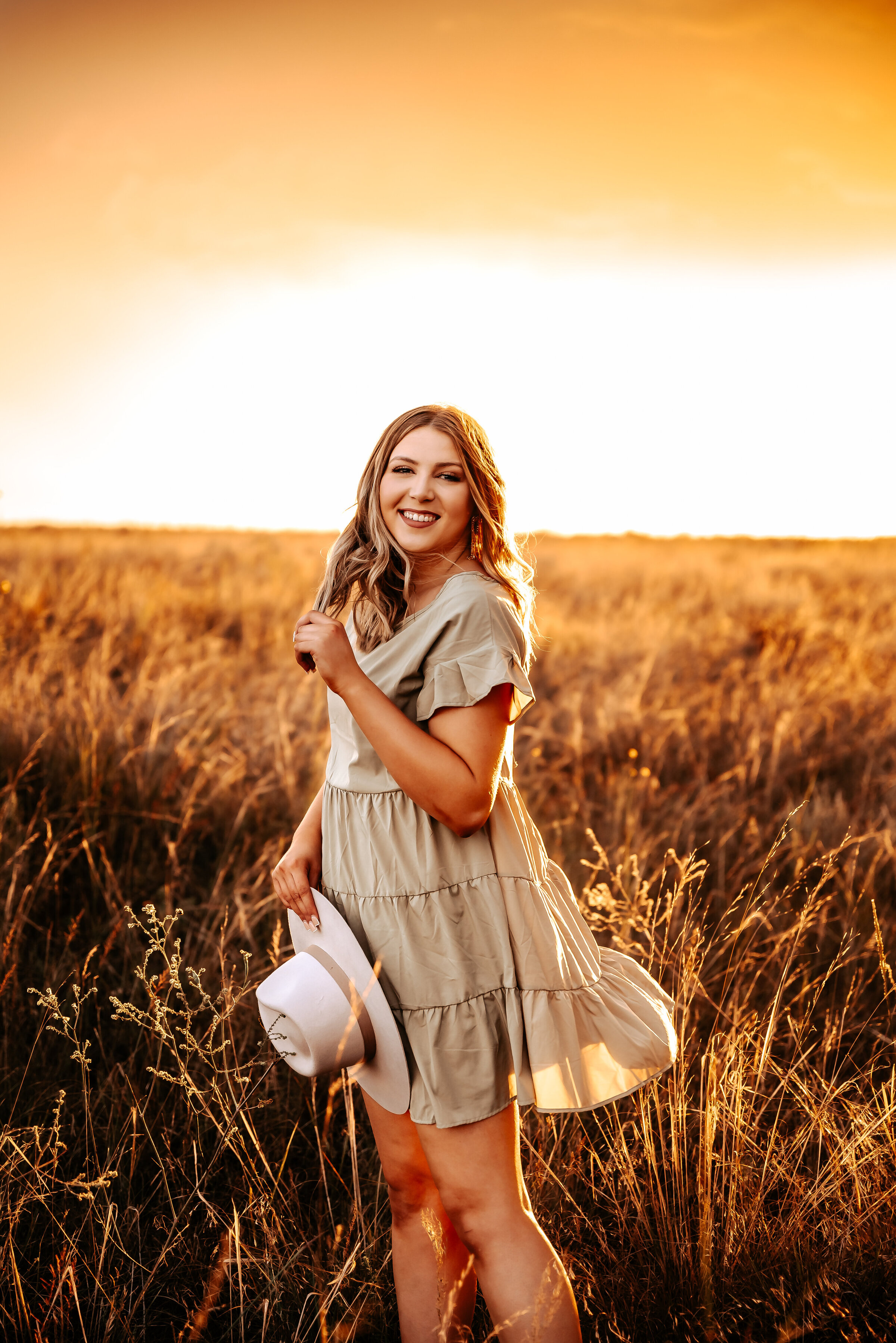 girl plays with hair and holds hat at sunset in Nebraska field