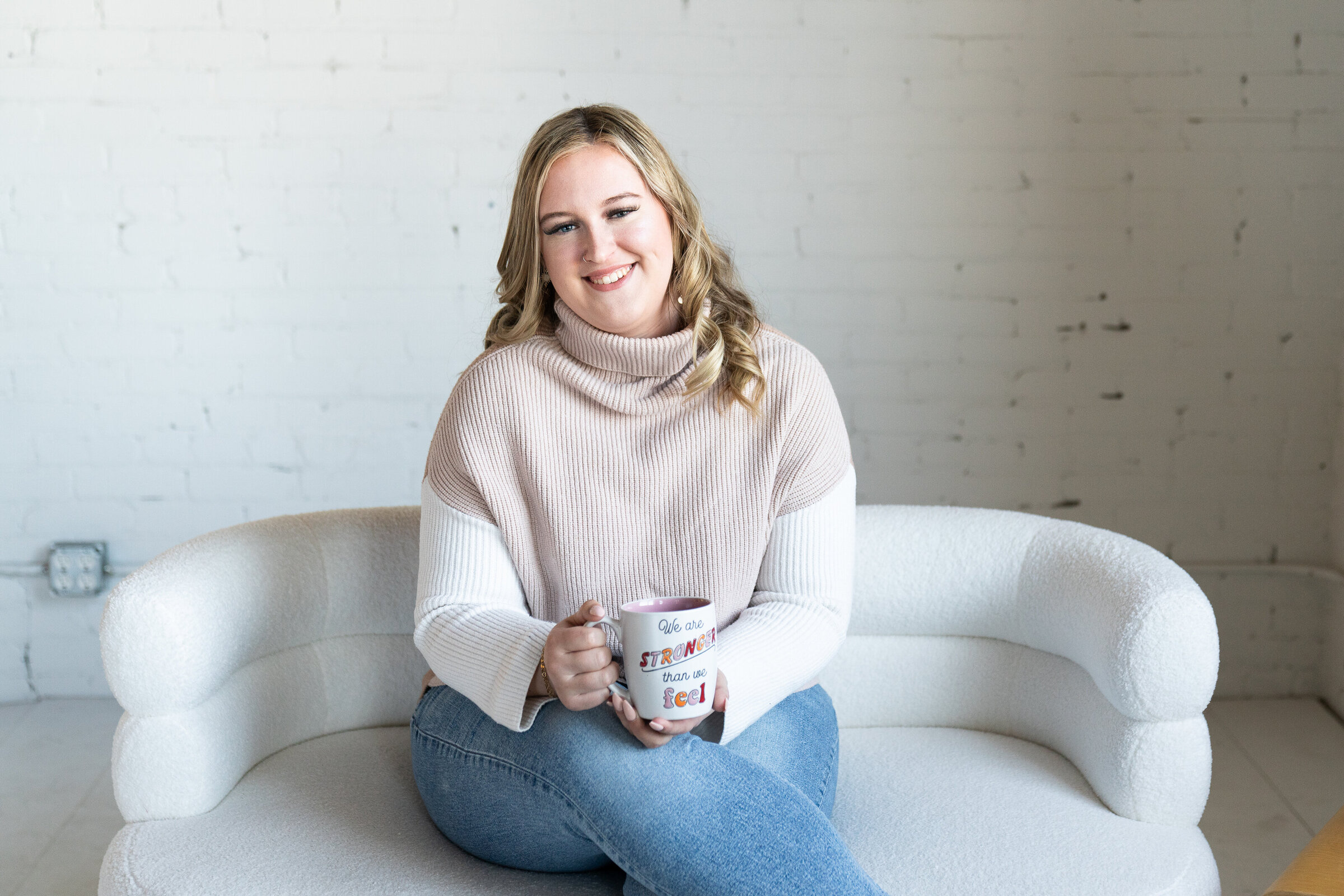 Woman sitting on a couch holding a coffee mug for her professional headshot photo shoot.