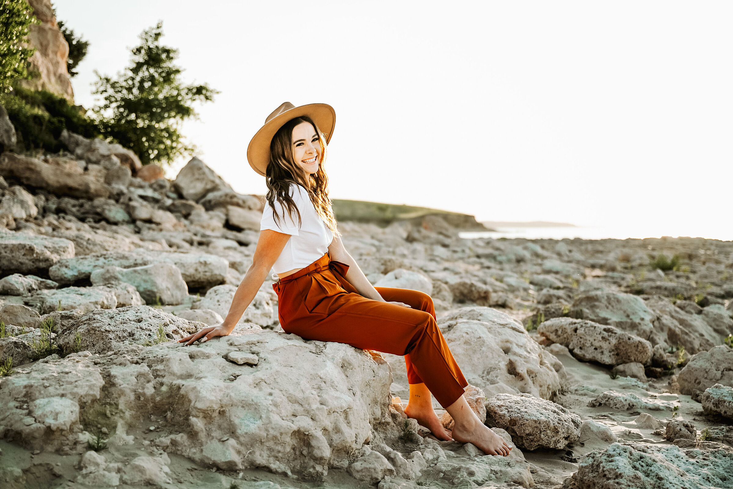 Senior girl sits on rocks at Ogallala Beach Lake McConaughy
