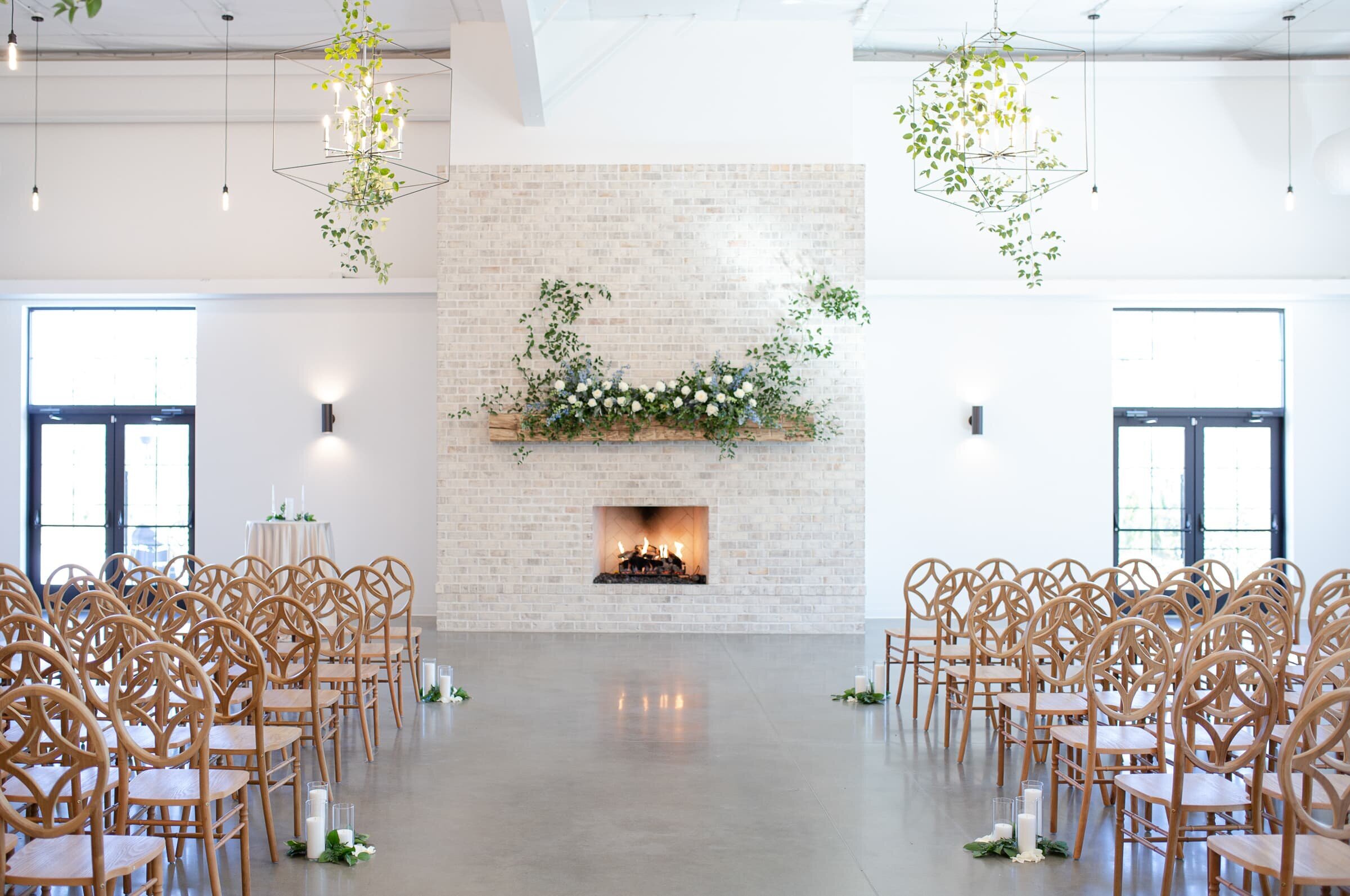 Indoor ceremony setup at the Maxwell Raleigh, NC. White and green floral arrangements, greenery ceiling installations, brown chiavari chairs.