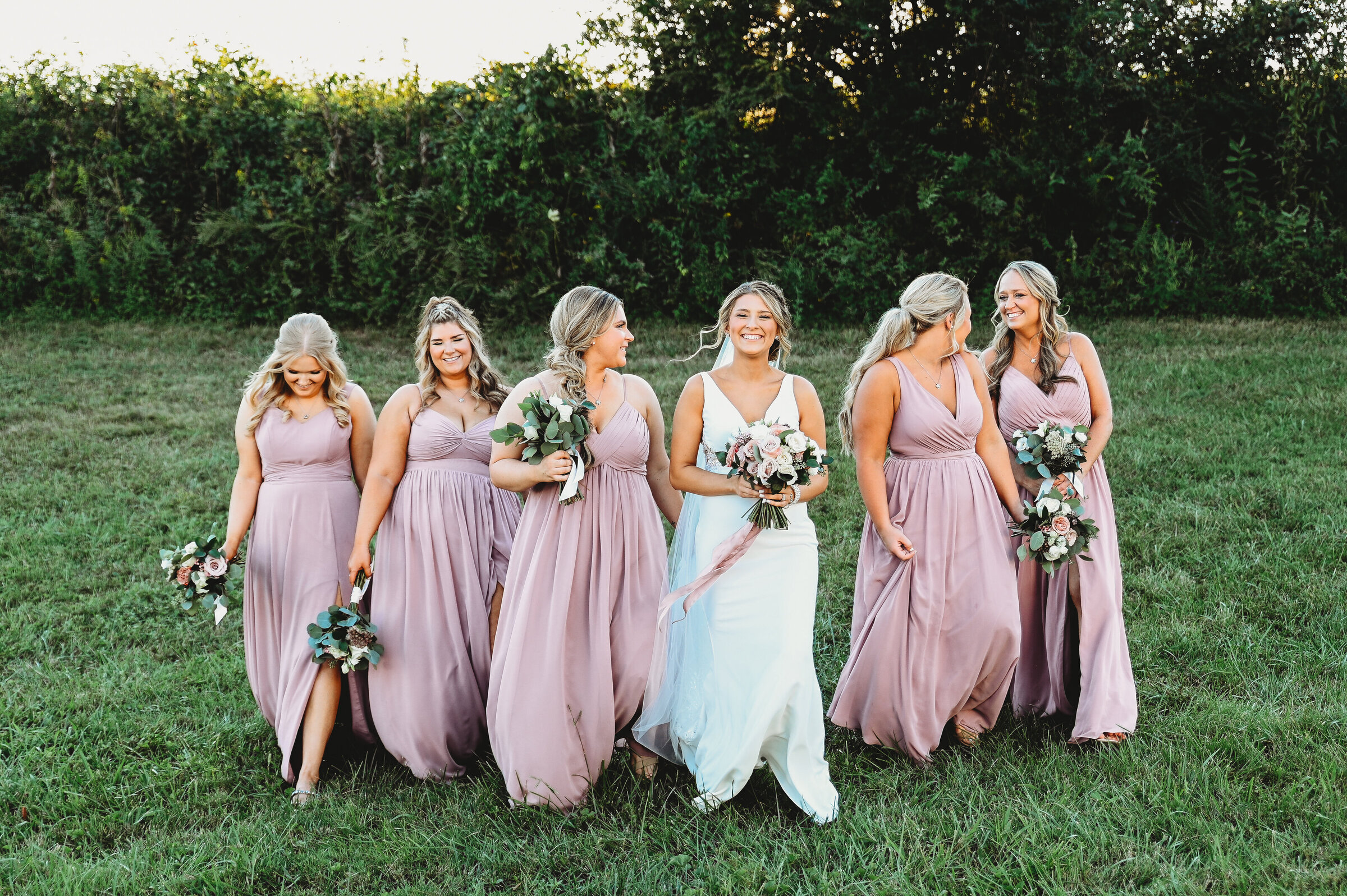 Bridesmaids wearing mauve walking with bride holding flowers