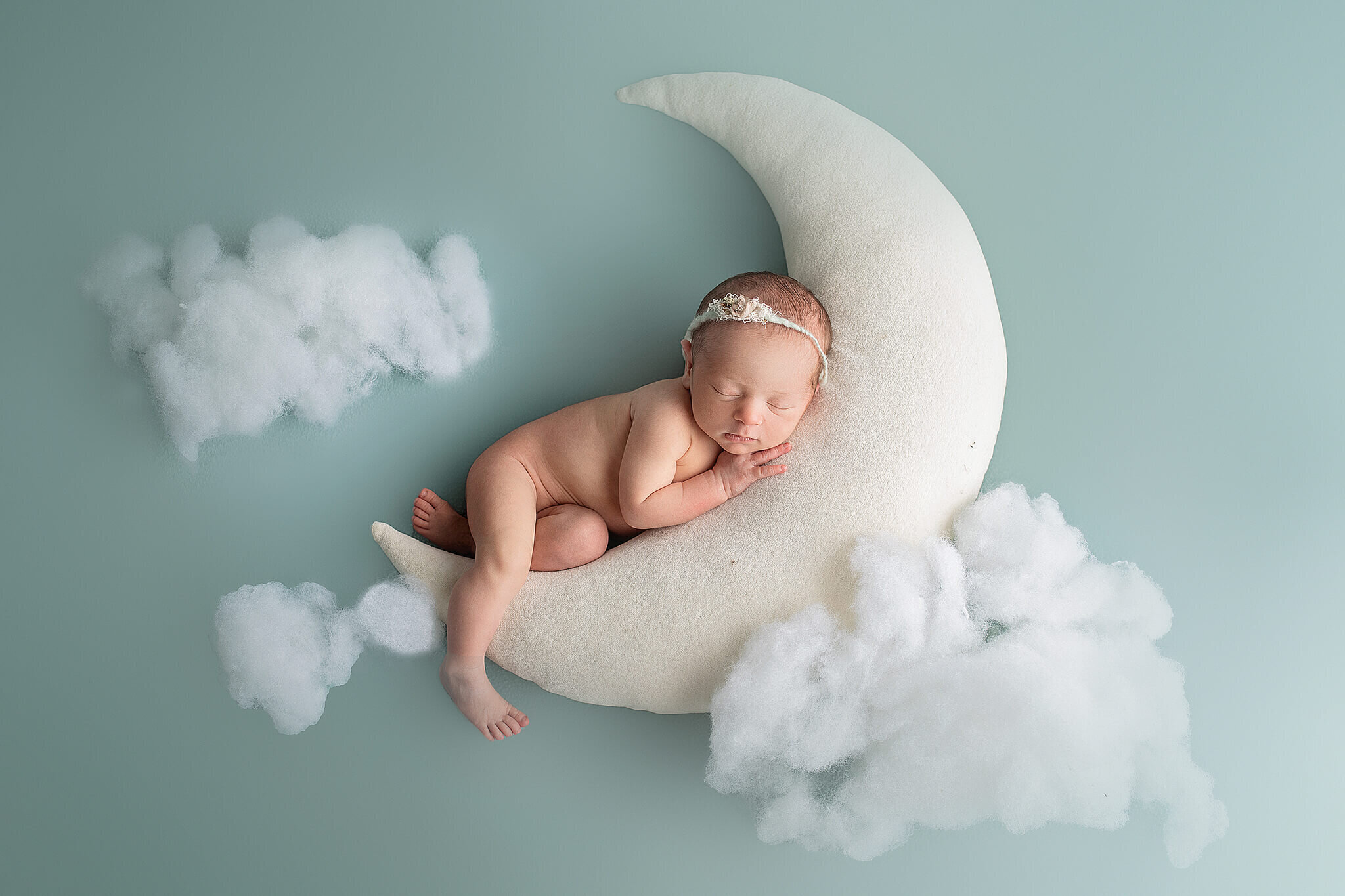 newborn baby girl snuggled on stuffed moon wtith clouds around  baby and moon