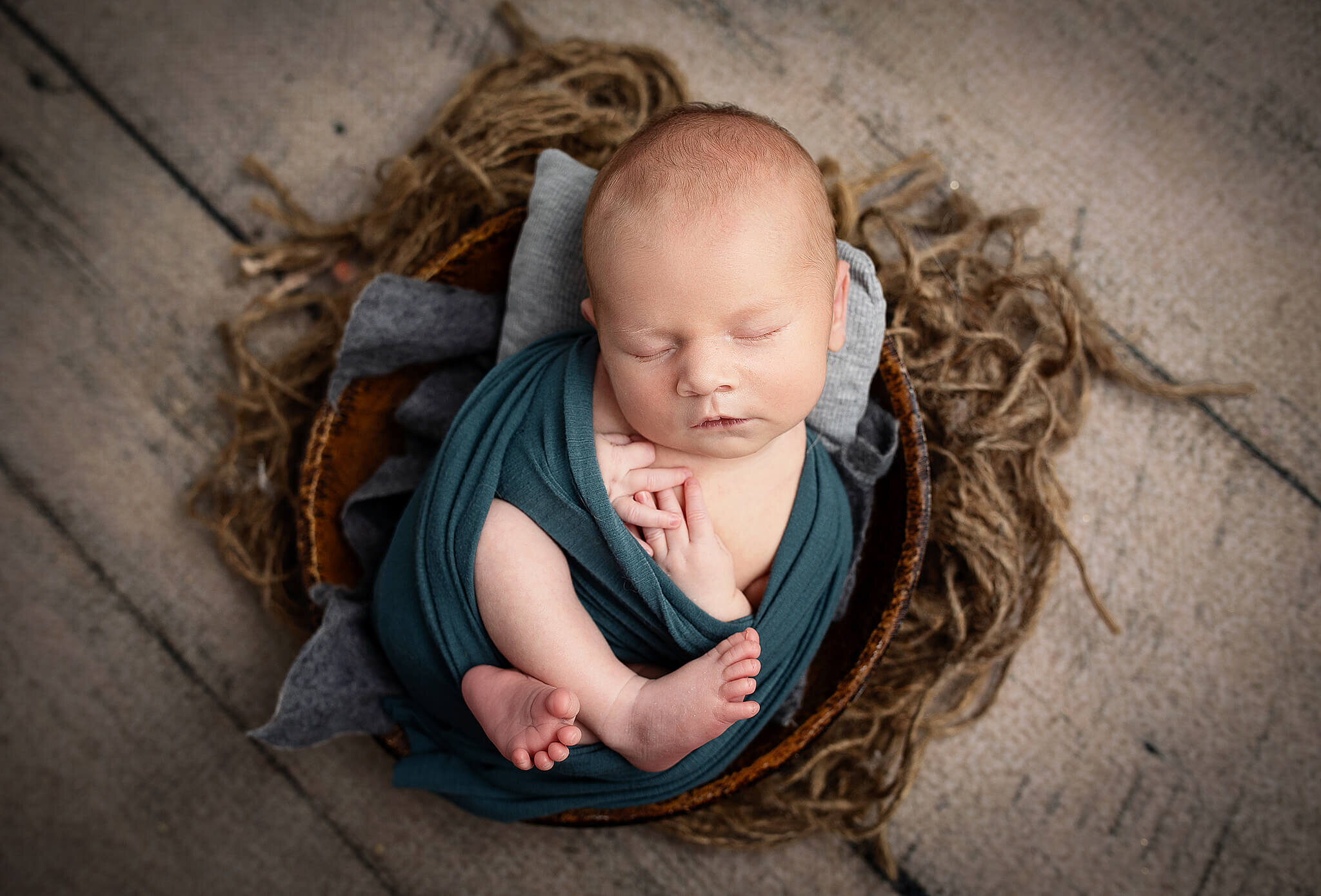newborn baby boy wrapped in a blue wrap and put in a little wooden bowl with textured  twine underneath bowl.