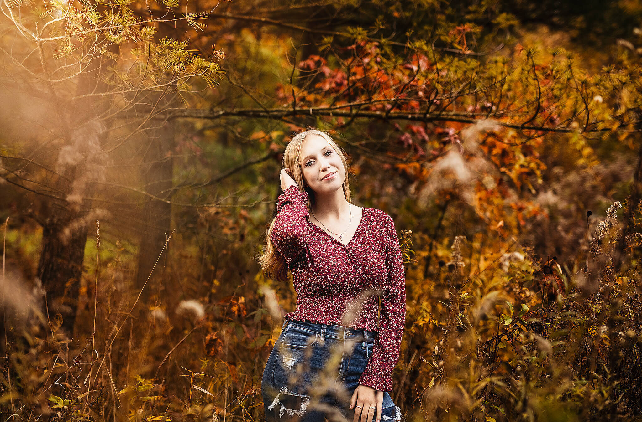 high school senior standing in front of fall colors posing in a red shirt and jeans at lowe volk park