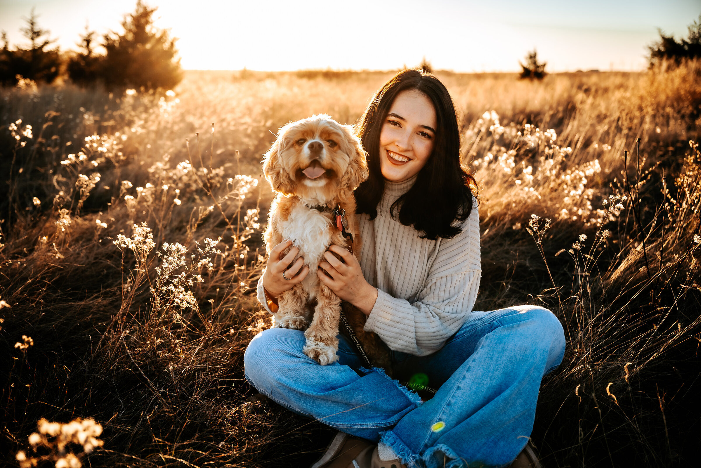 girl sits with her dog in long grass lit up by the sun