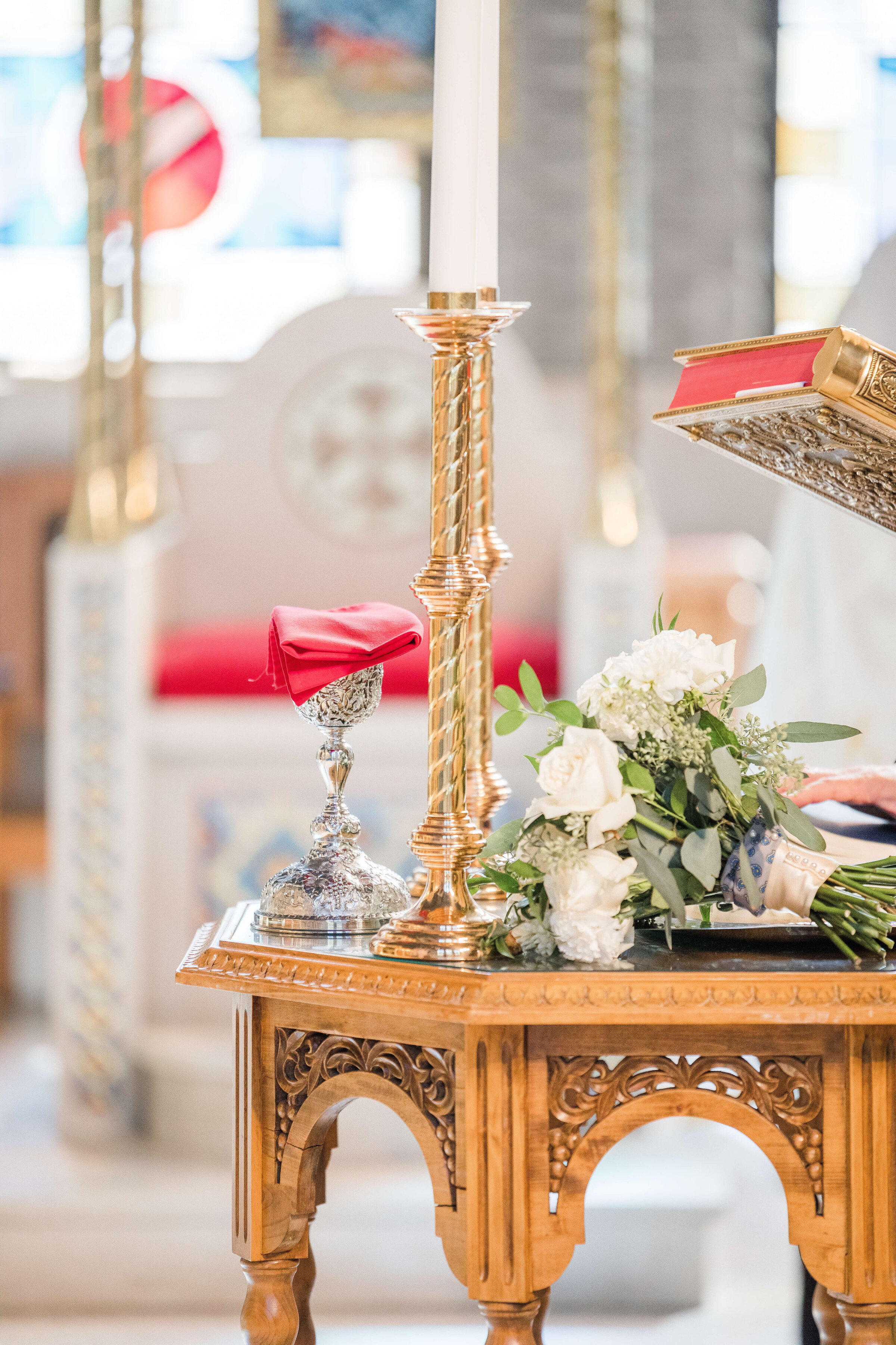 A tall gold candlestick sits on a gold table in a church with bright windows in the back