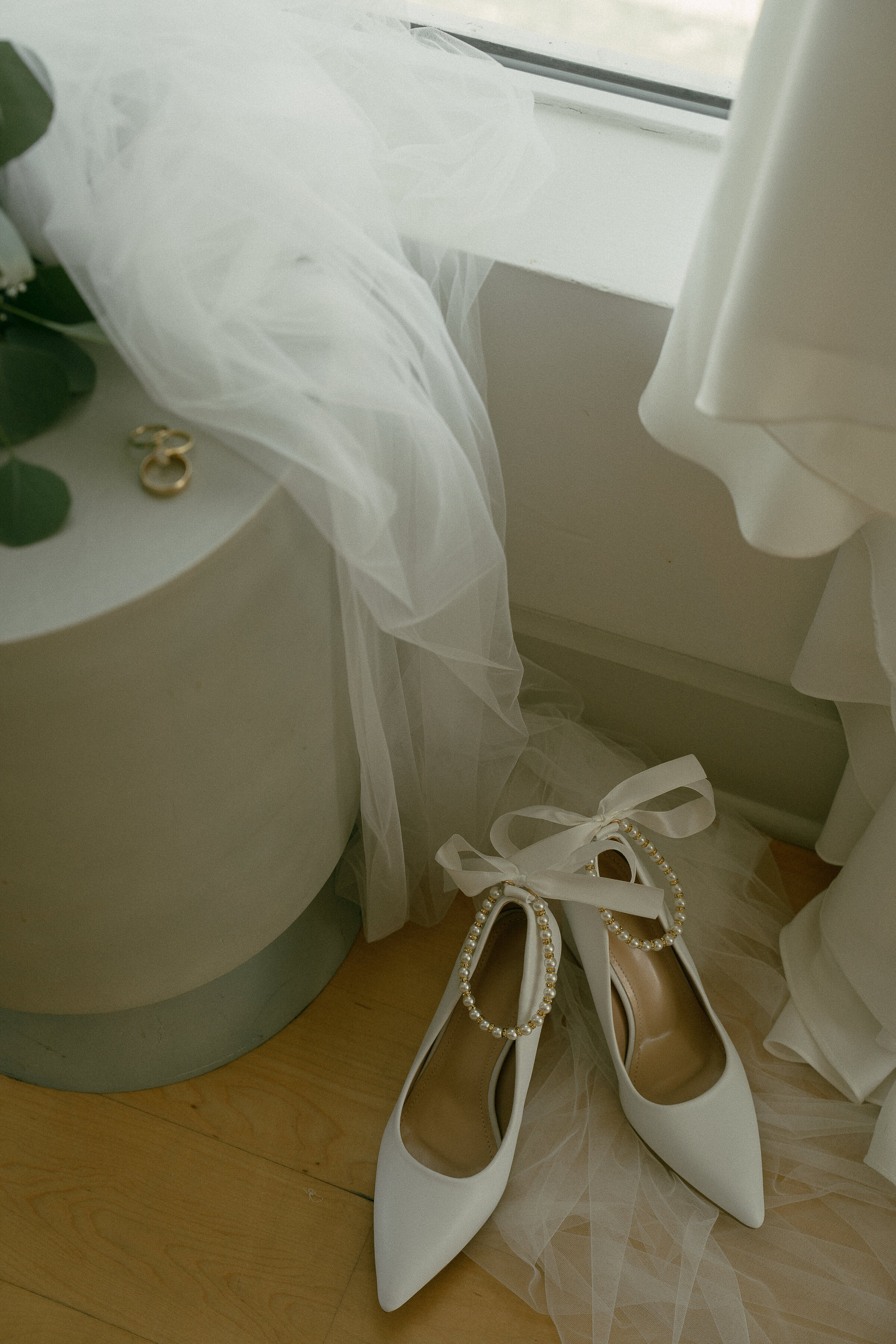 Wedding shoes with pearls and ribbons next to a flowing veil on the floor.