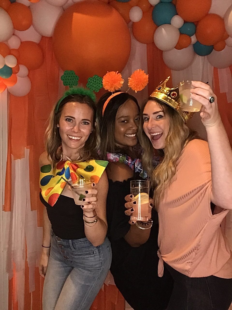 Girls cheersing together with an Orange photobooth background