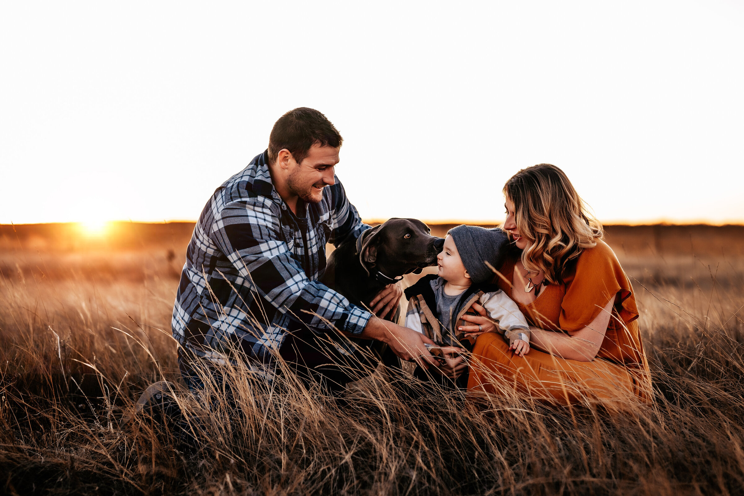 Mom, dad, and son sit next to their dog in a field
