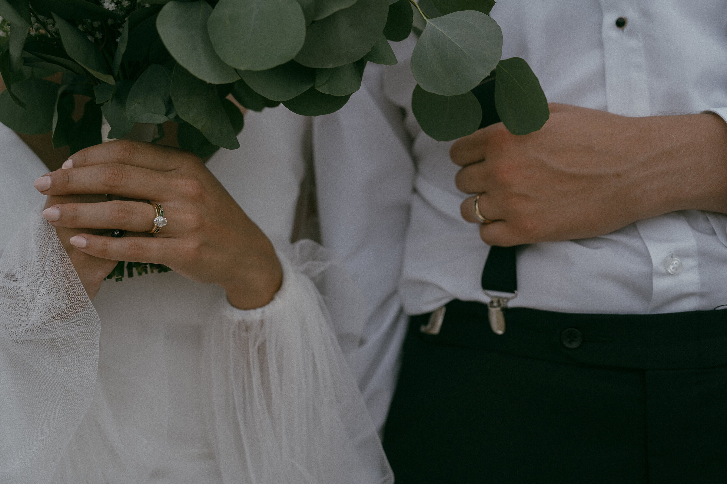Detail shot of wedding rings and hands holding a bouquet.