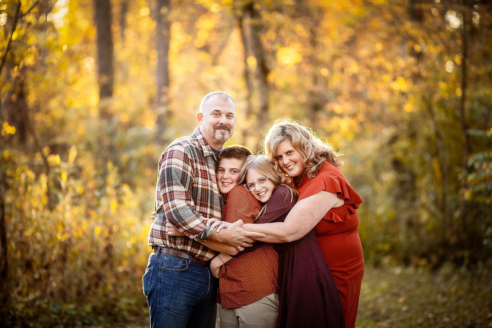 Mom and dad with two children hugging for photo in woods