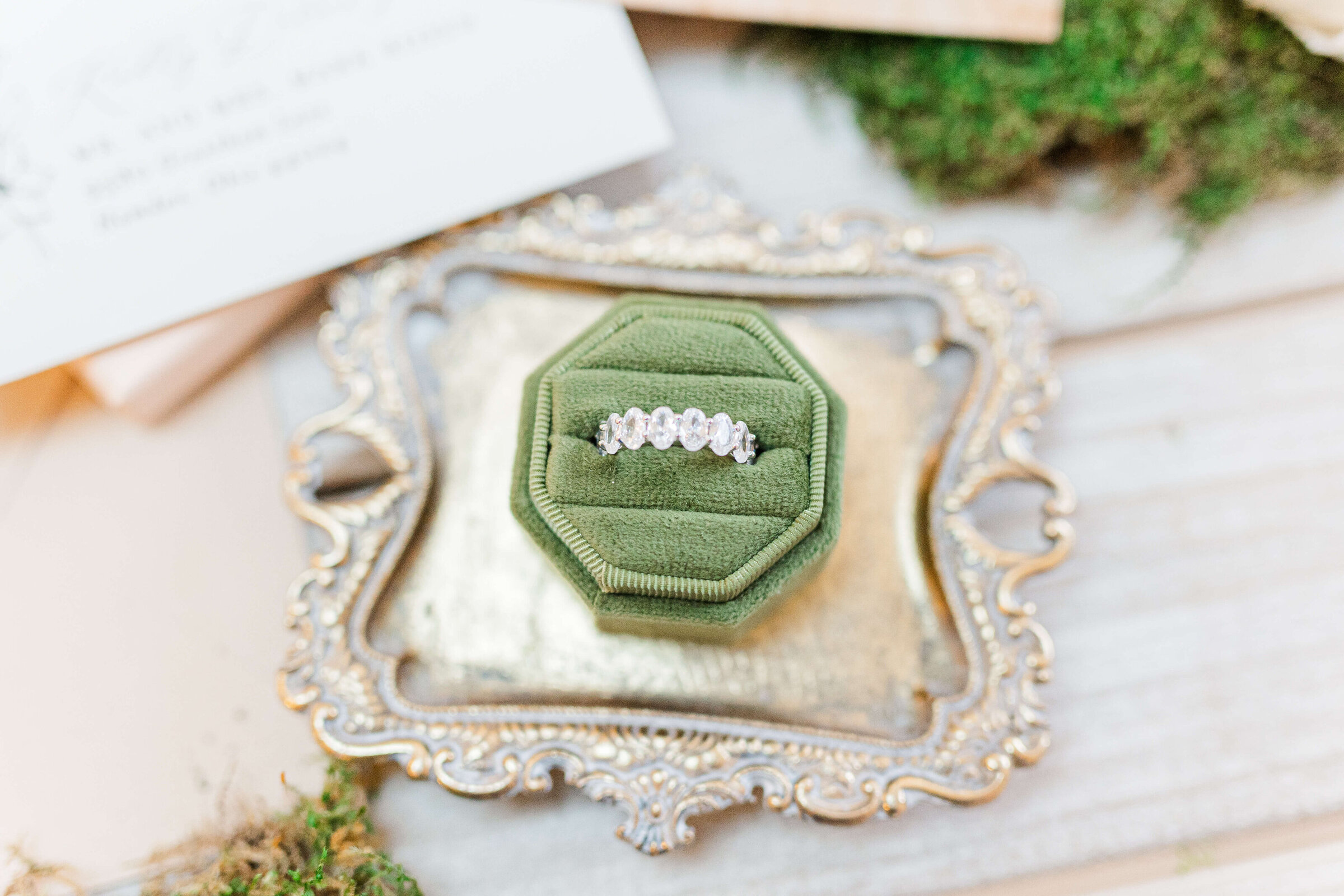 A gold tray that has a green wedding box with a wedding ring in it