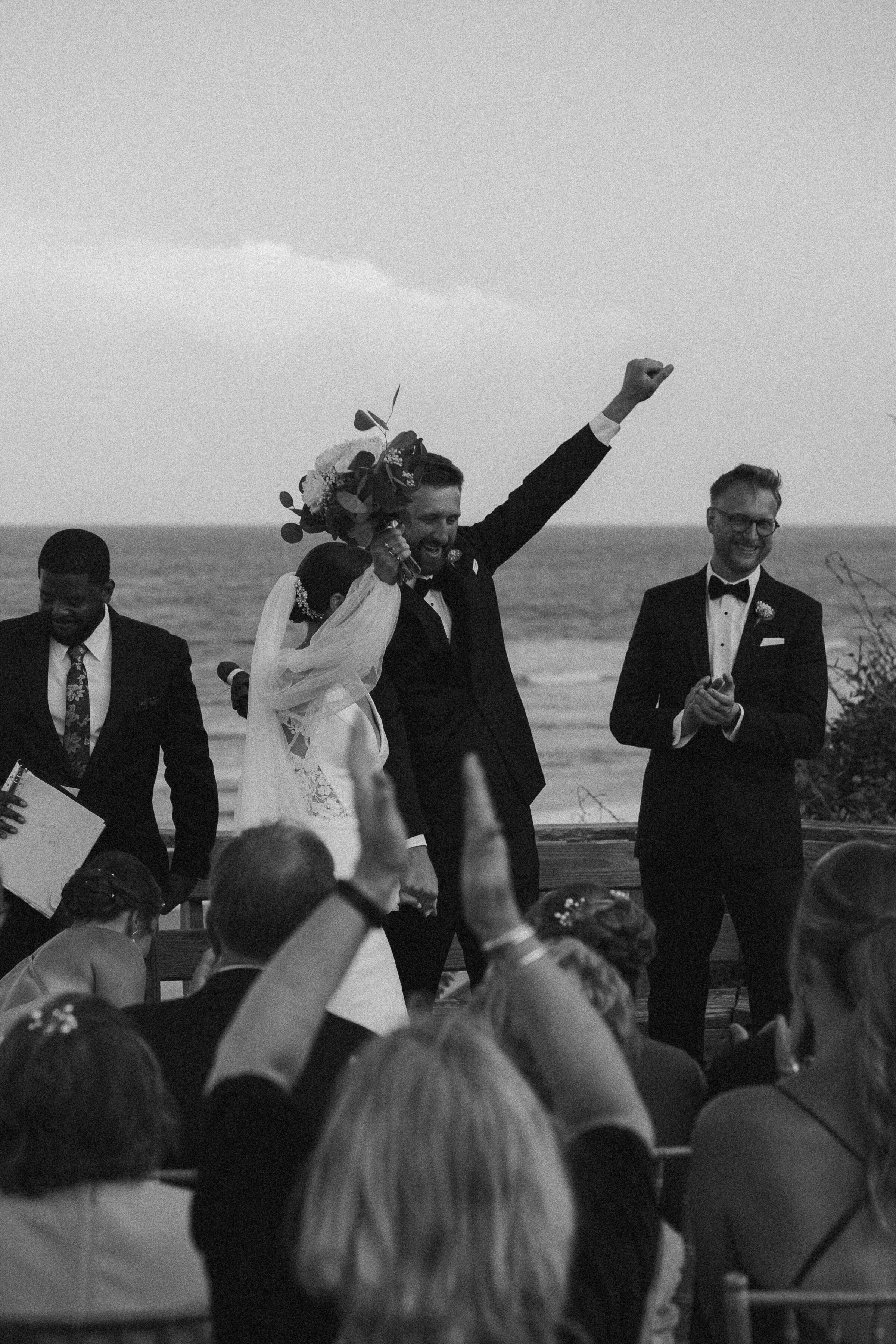 Bride and groom with raised fist, cheered by guests