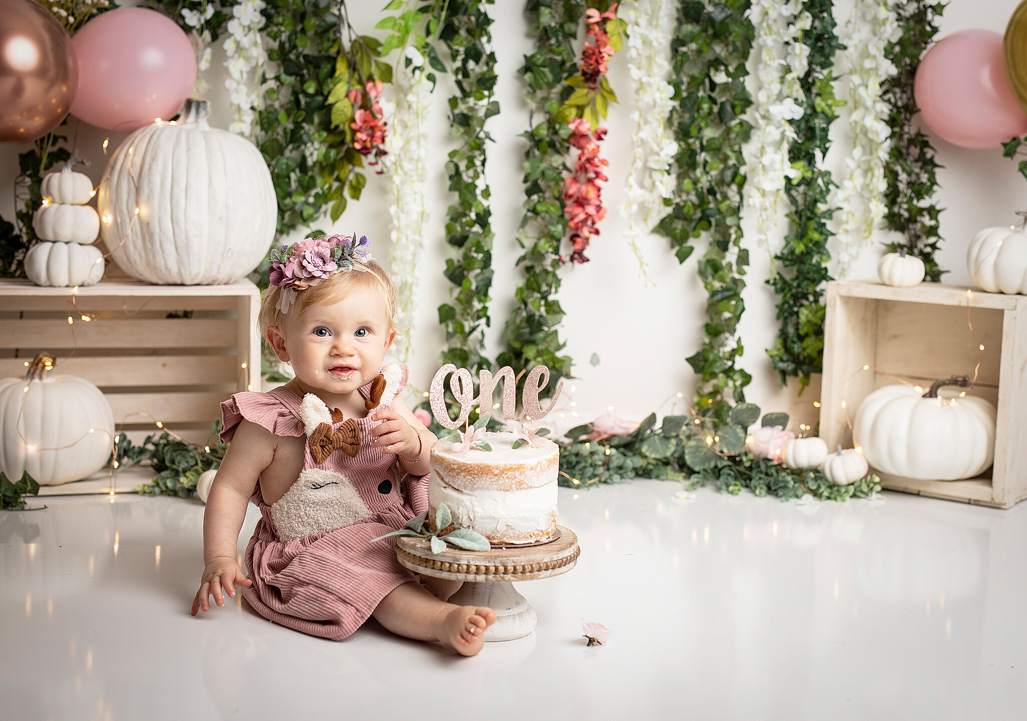 BAby smashing cake . wearing pink dress with flowers on the background, and pumpkins dotted as well