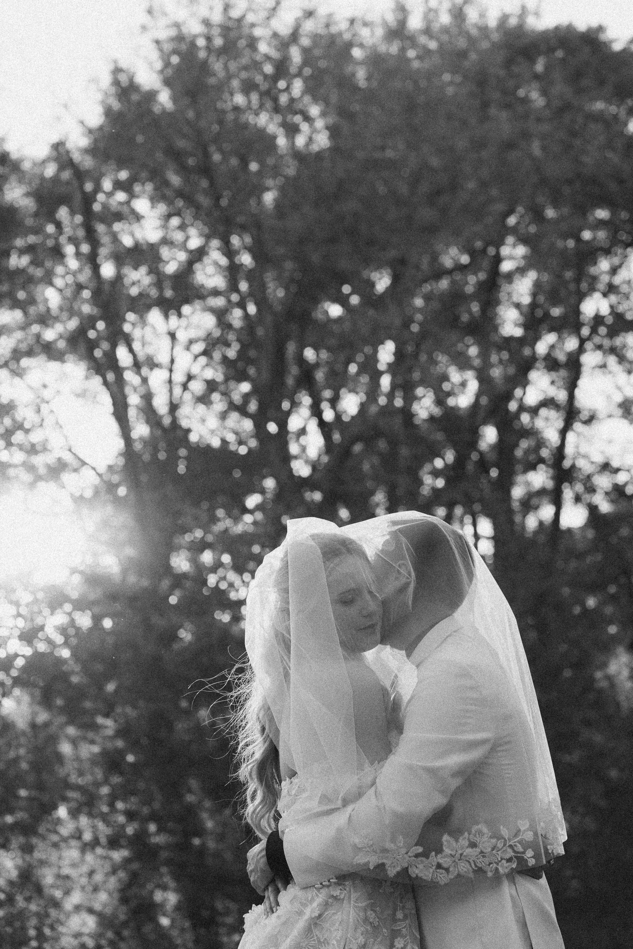 Bride and groom embrace under the veil in monochrome.