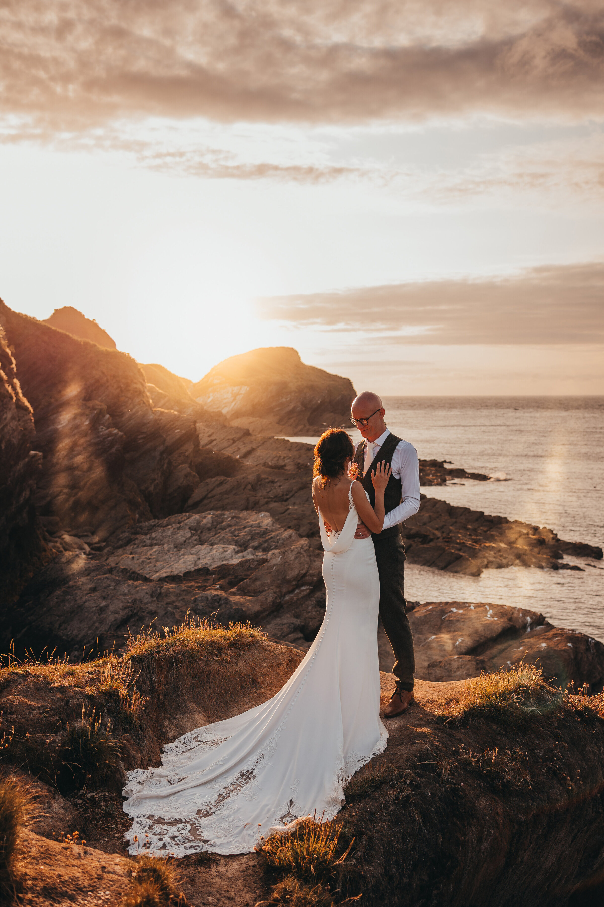 couple standing on rocks by the ocean during sunset