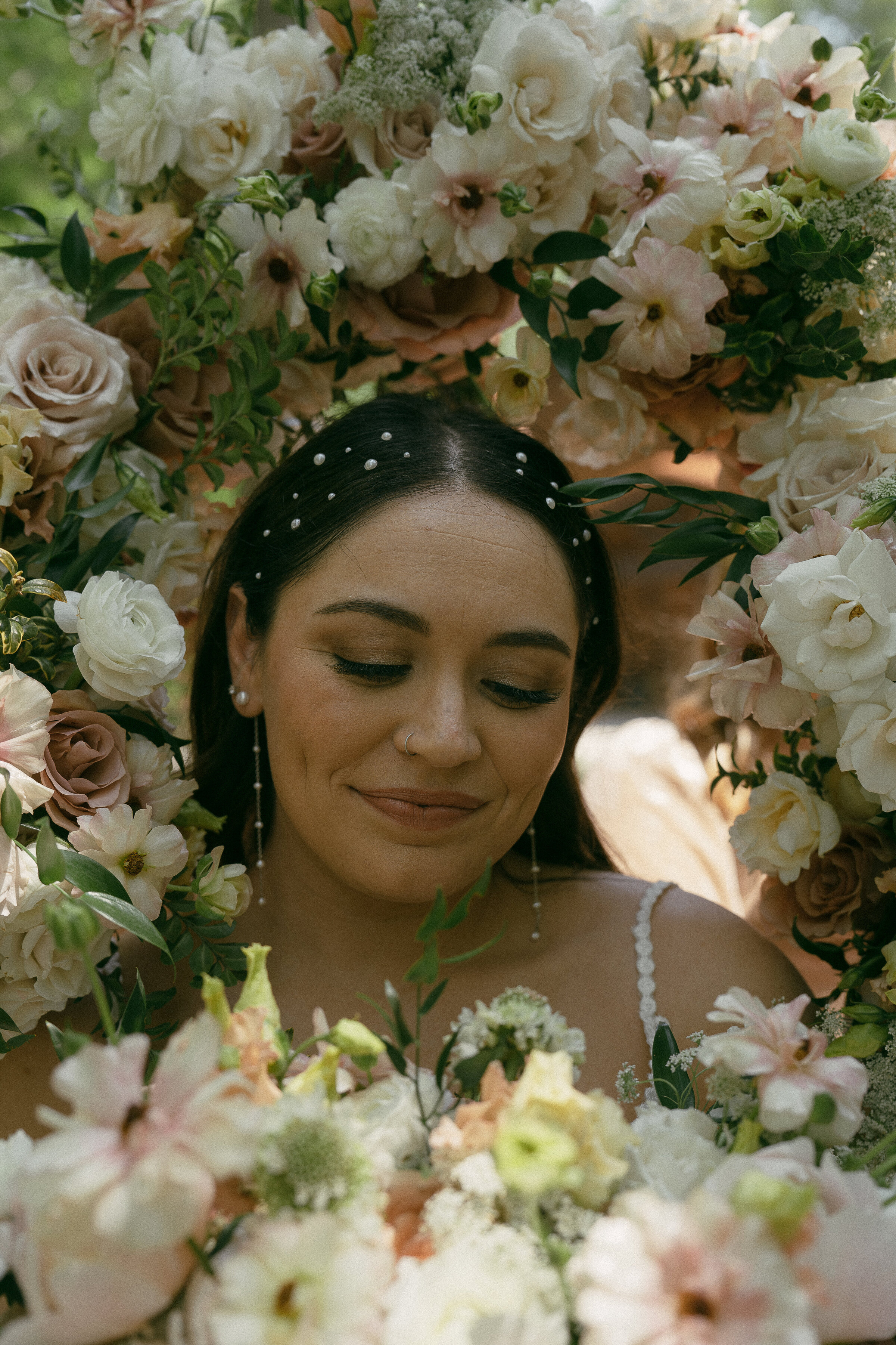 Bride smiling surrounded by floral arrangement, intimate wedding portrait.