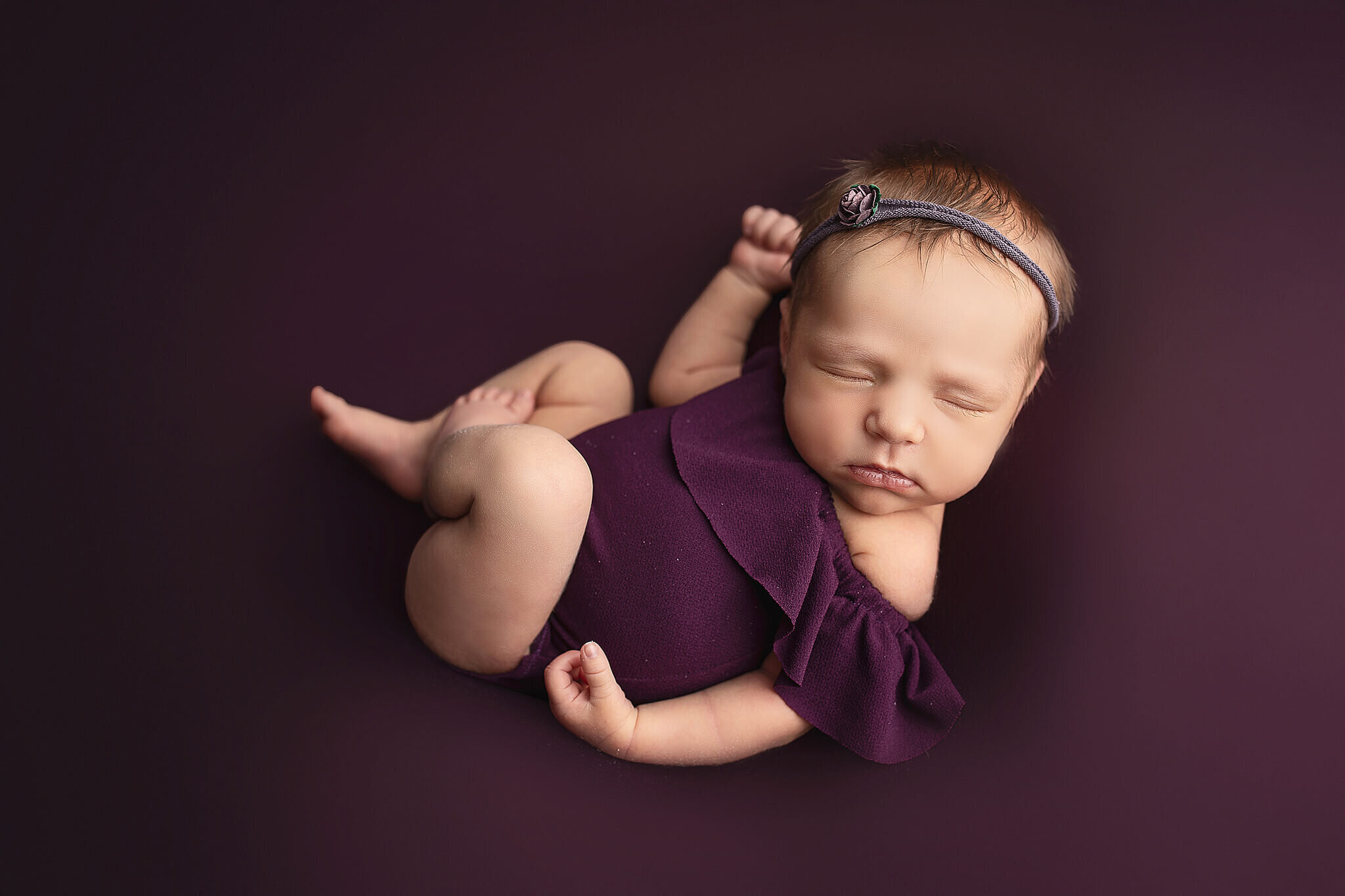 newborn baby girl on purple blanket in a cute purple outfit while sweetly sleeping on her back