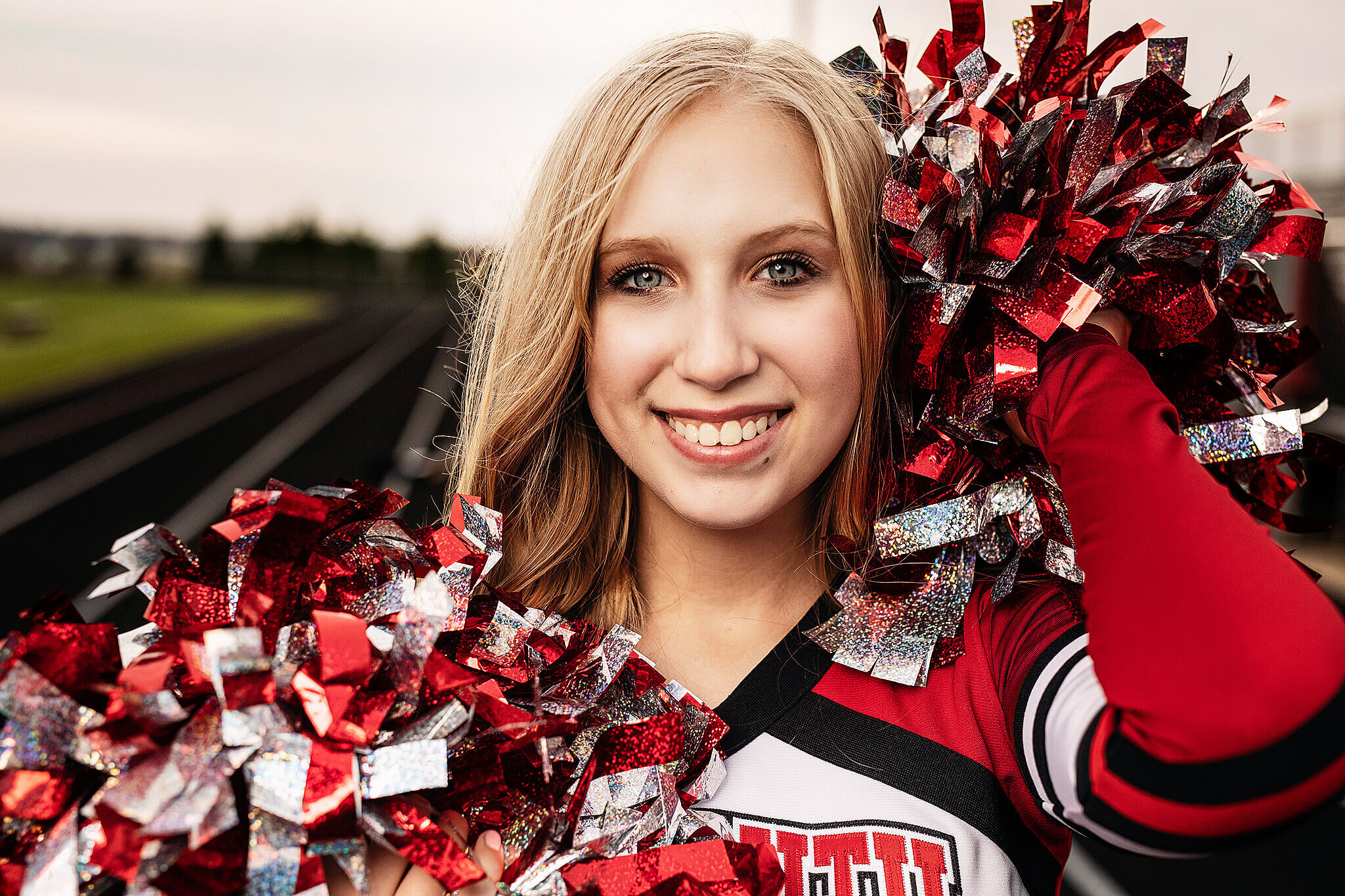 high school senior cheerleader holding red and silver pompoms  on track