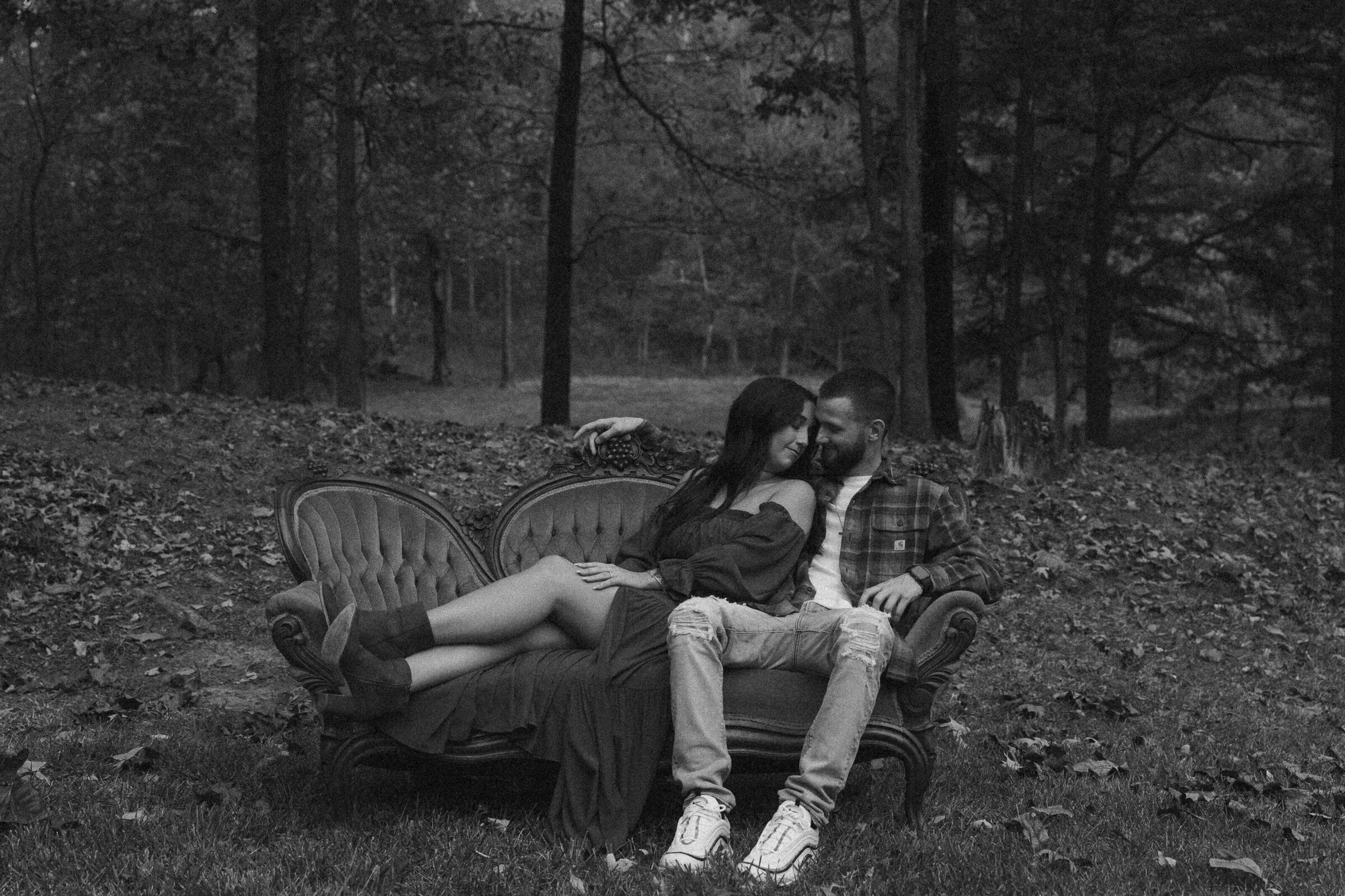 Couple embracing on a vintage sofa outdoors, candid black and white photo.
