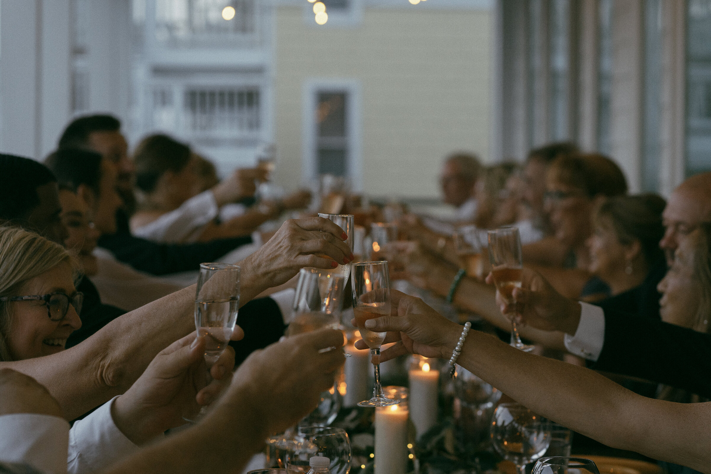 Guests raising glasses for a toast at a dimly lit indoor wedding reception.